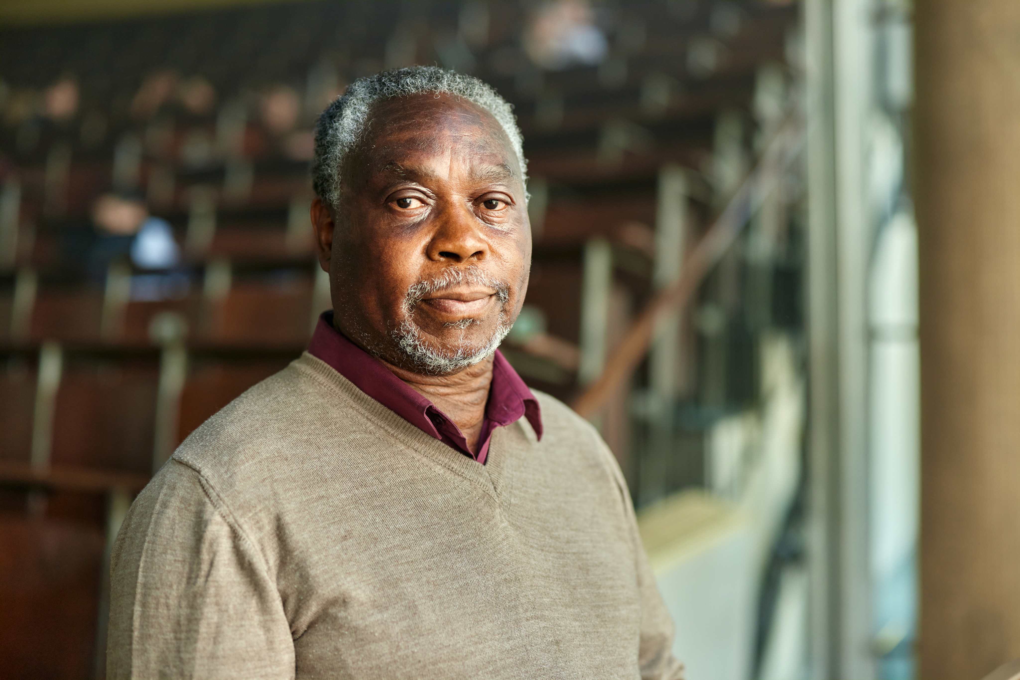 African American man with gray hair wearing tan sweater and burgundy collar