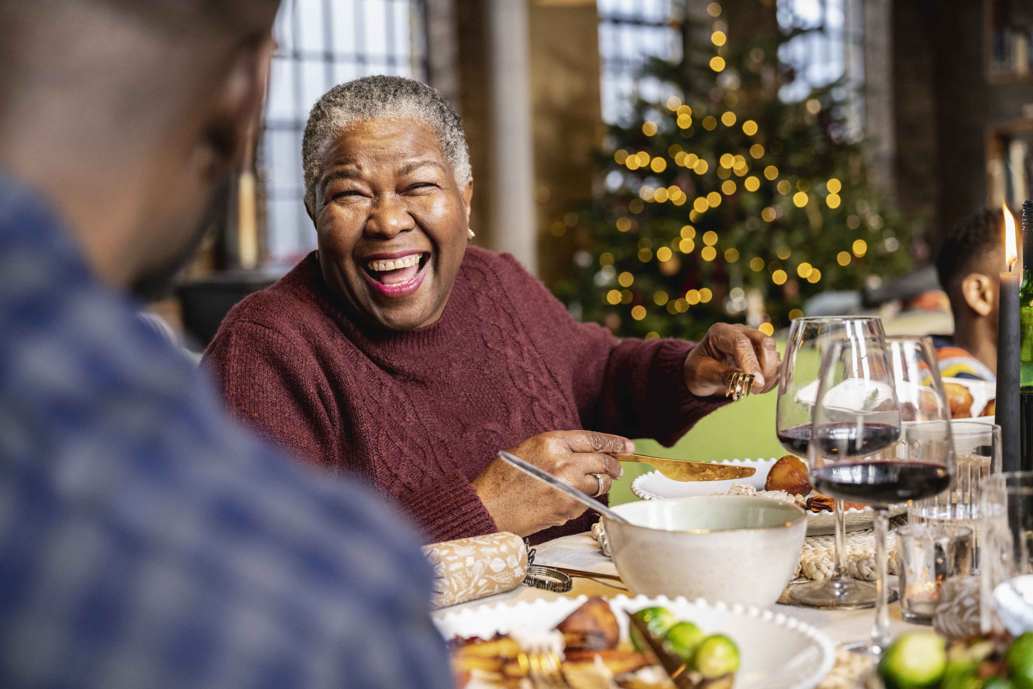 Elderly woman laughing at Christmas dinner table with family