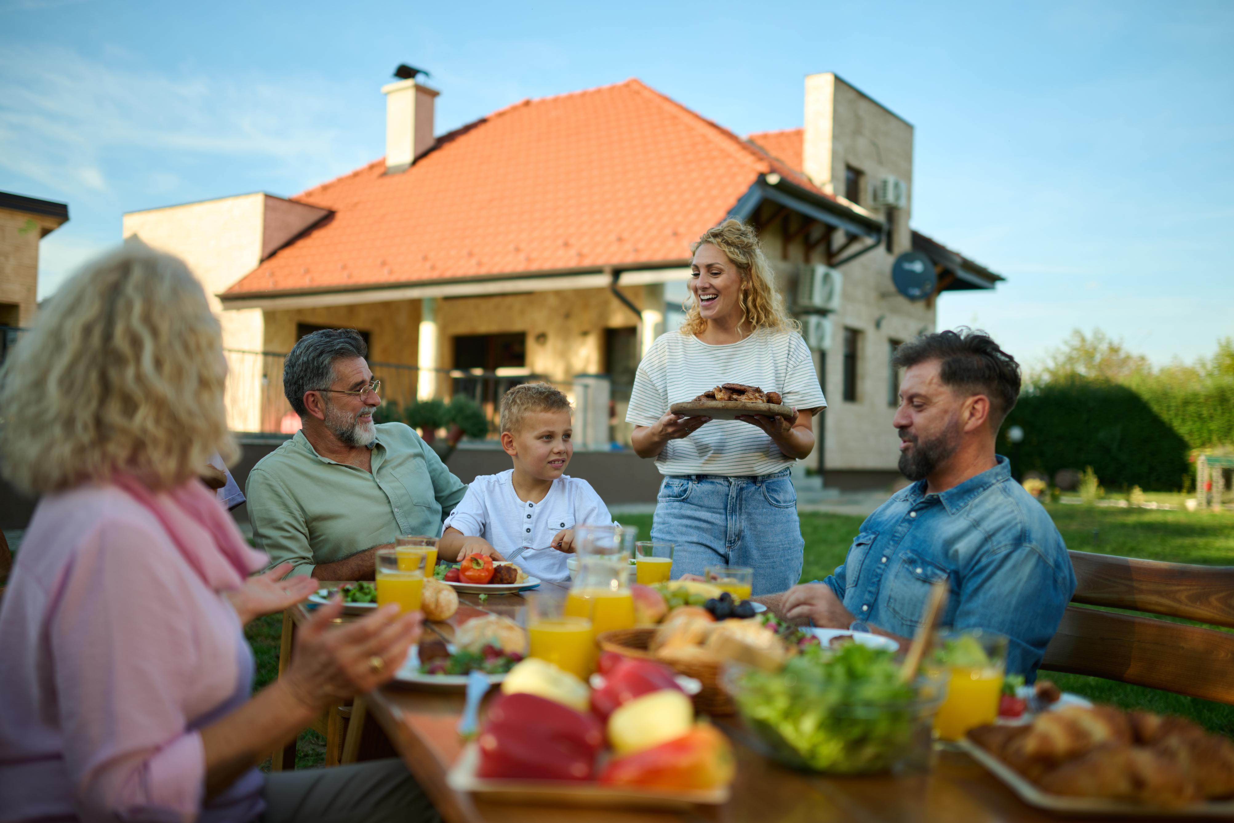 Family enjoying outdoor meal together in backyard with woman serving food