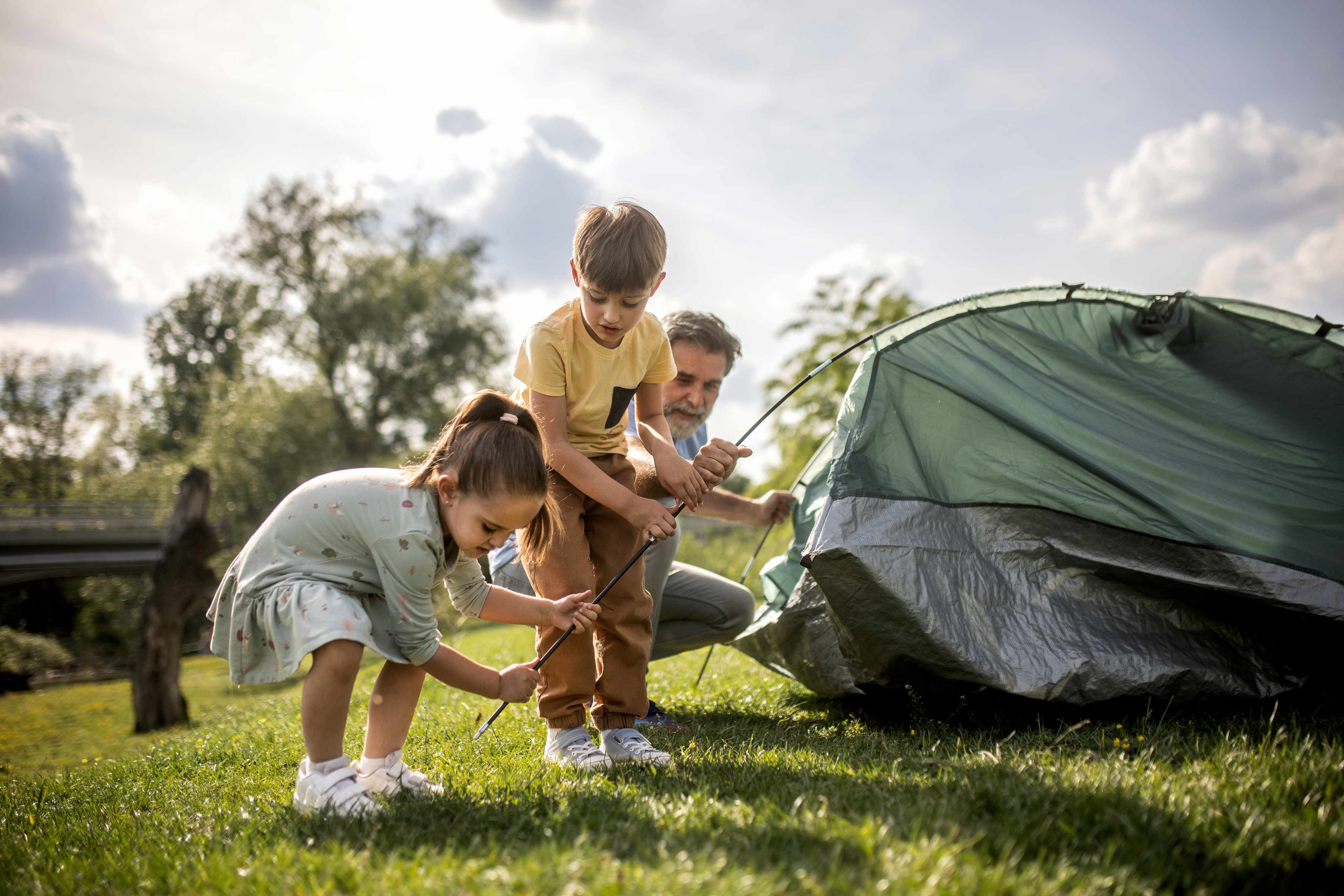 Family setting up tent together on sunny camping trip outdoors