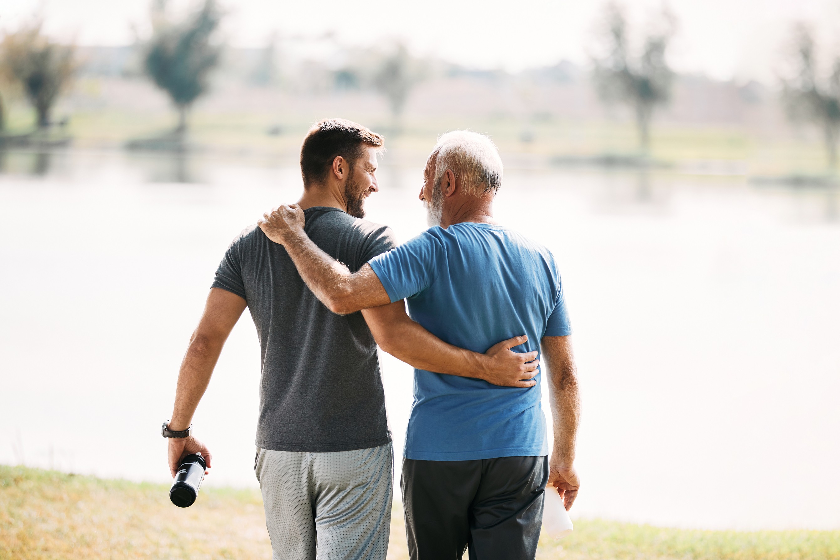 Father and son embracing while exercising together by a lake