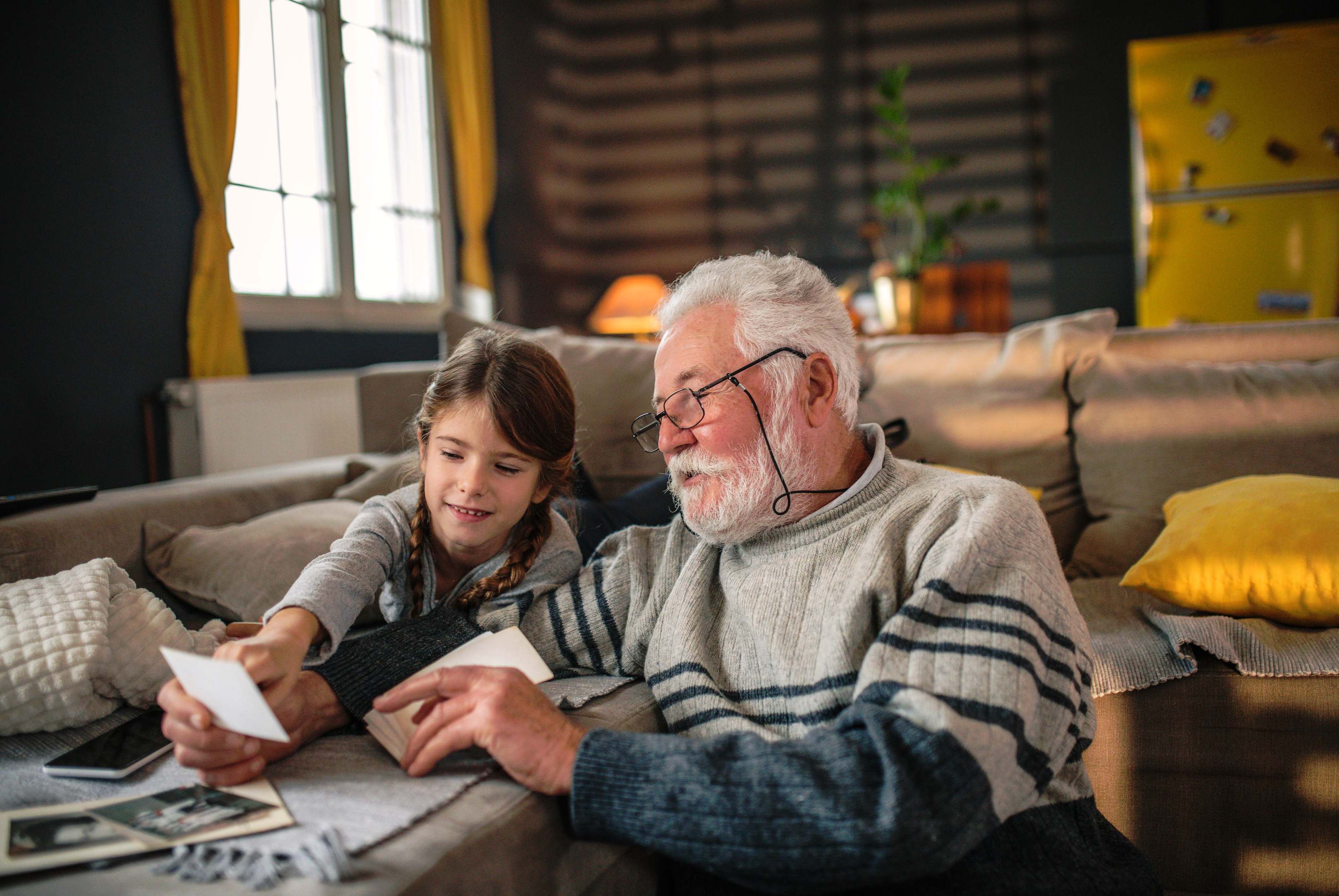 grandfather and granddaughter looking at photos together on couch