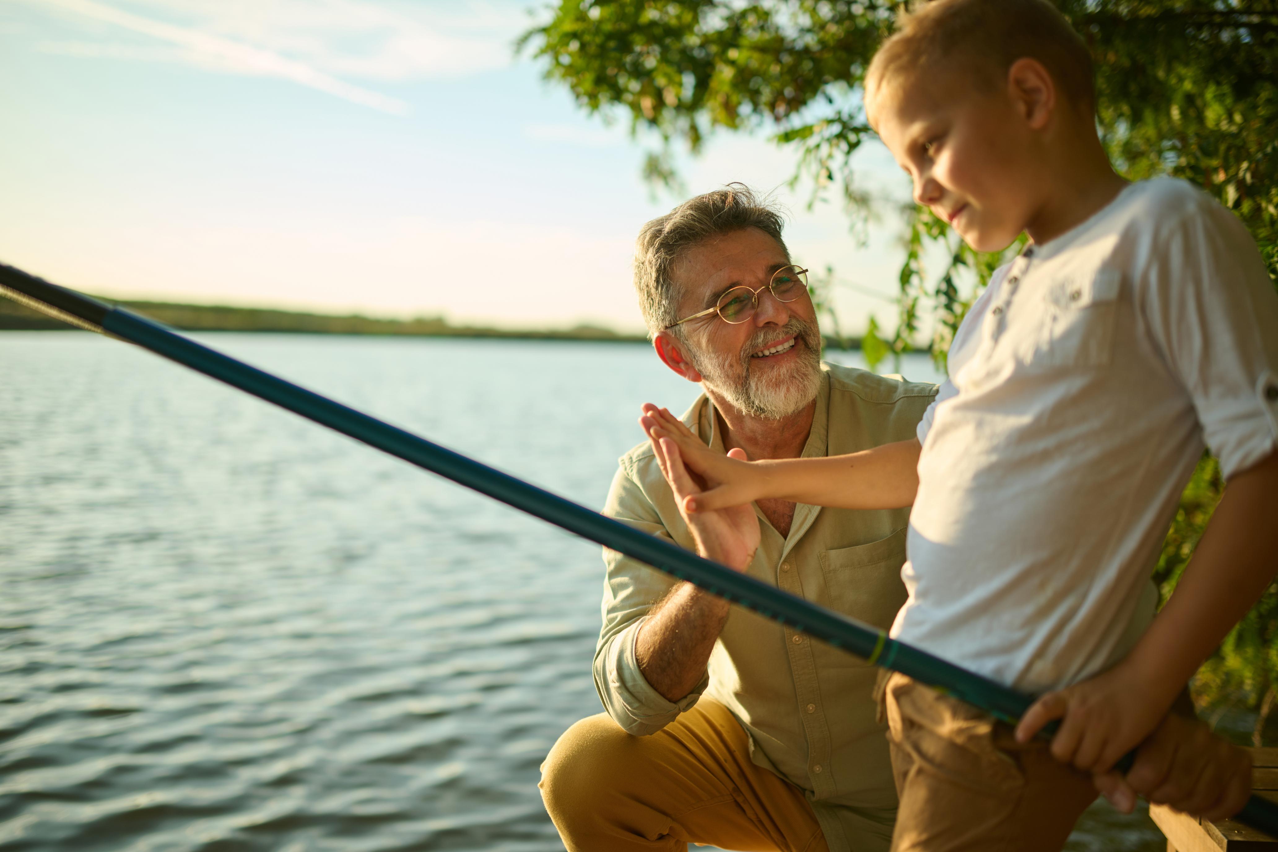 grandfather and grandson fishing together by the lake at sunset