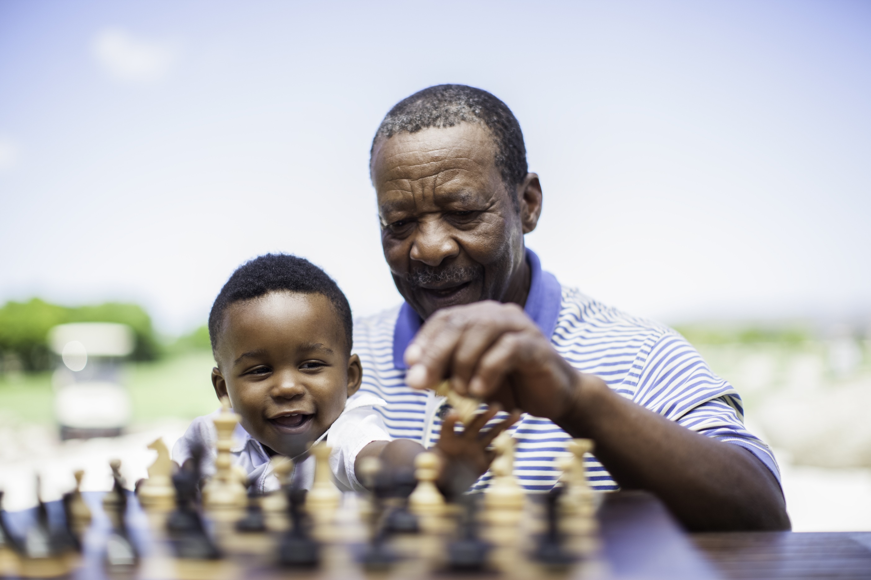 Grandfather teaching young child to play chess outdoors