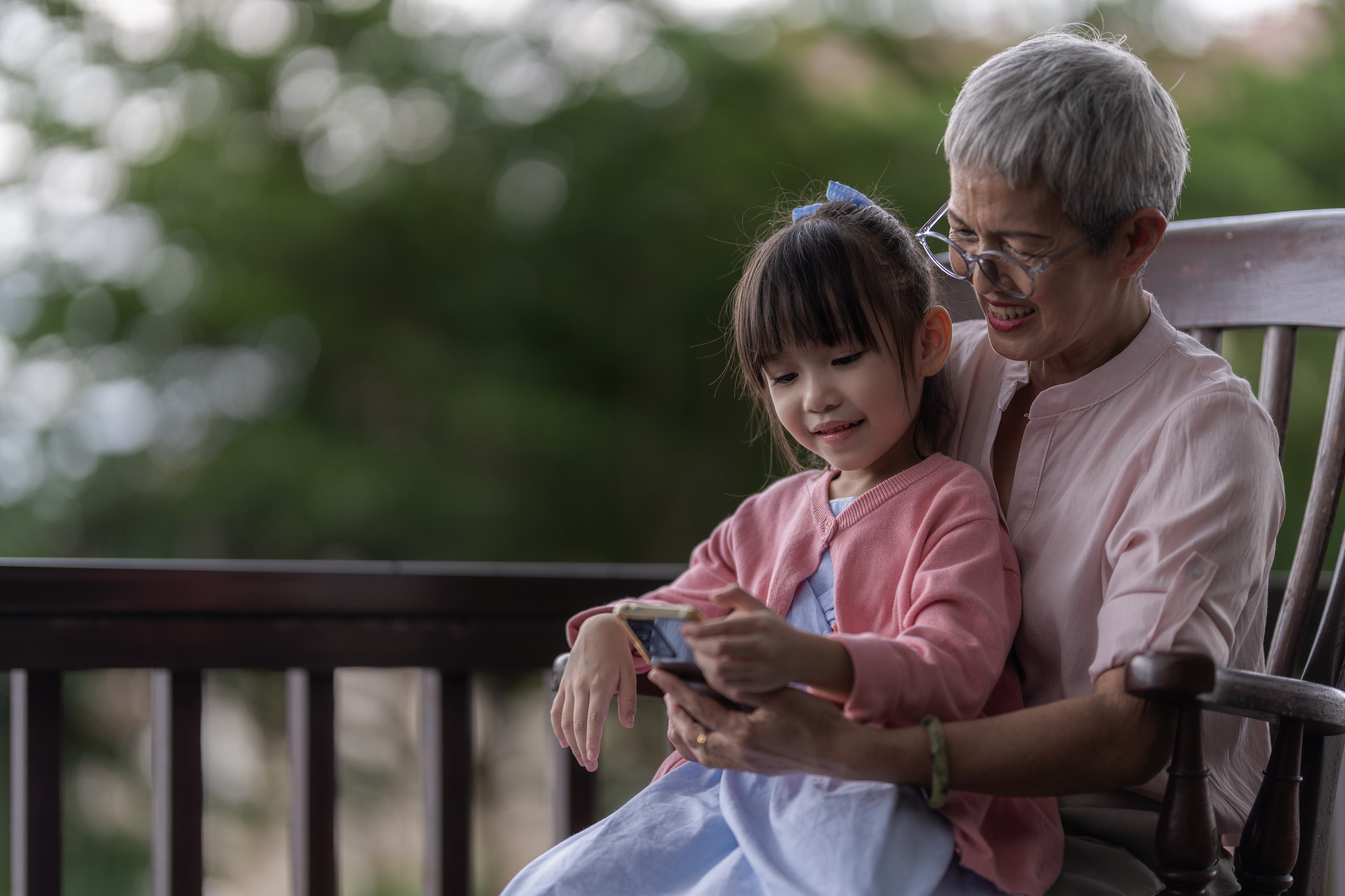 Grandmother and granddaughter sitting together looking at phone outdoors