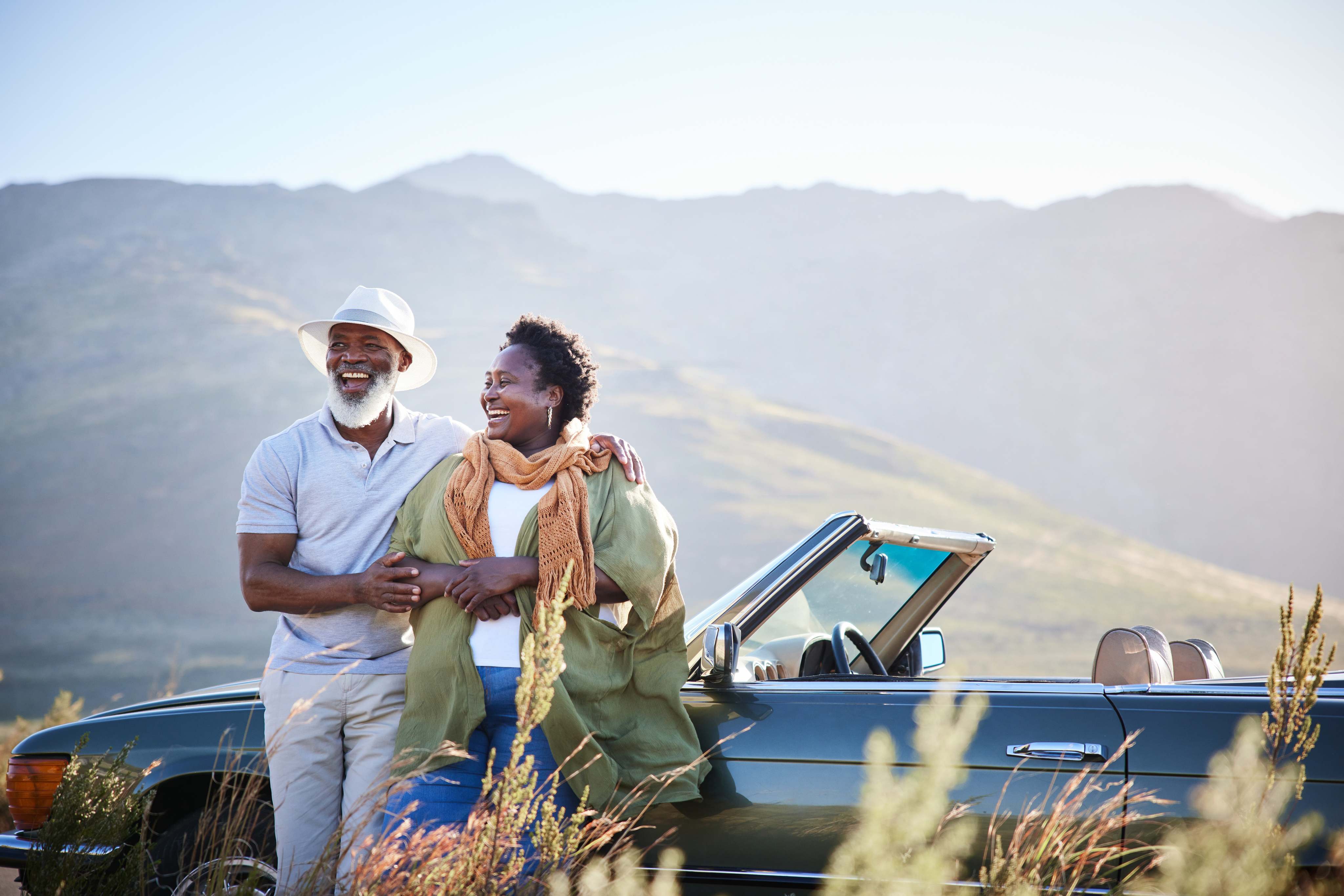 Happy couple embracing beside convertible car with mountain landscape background