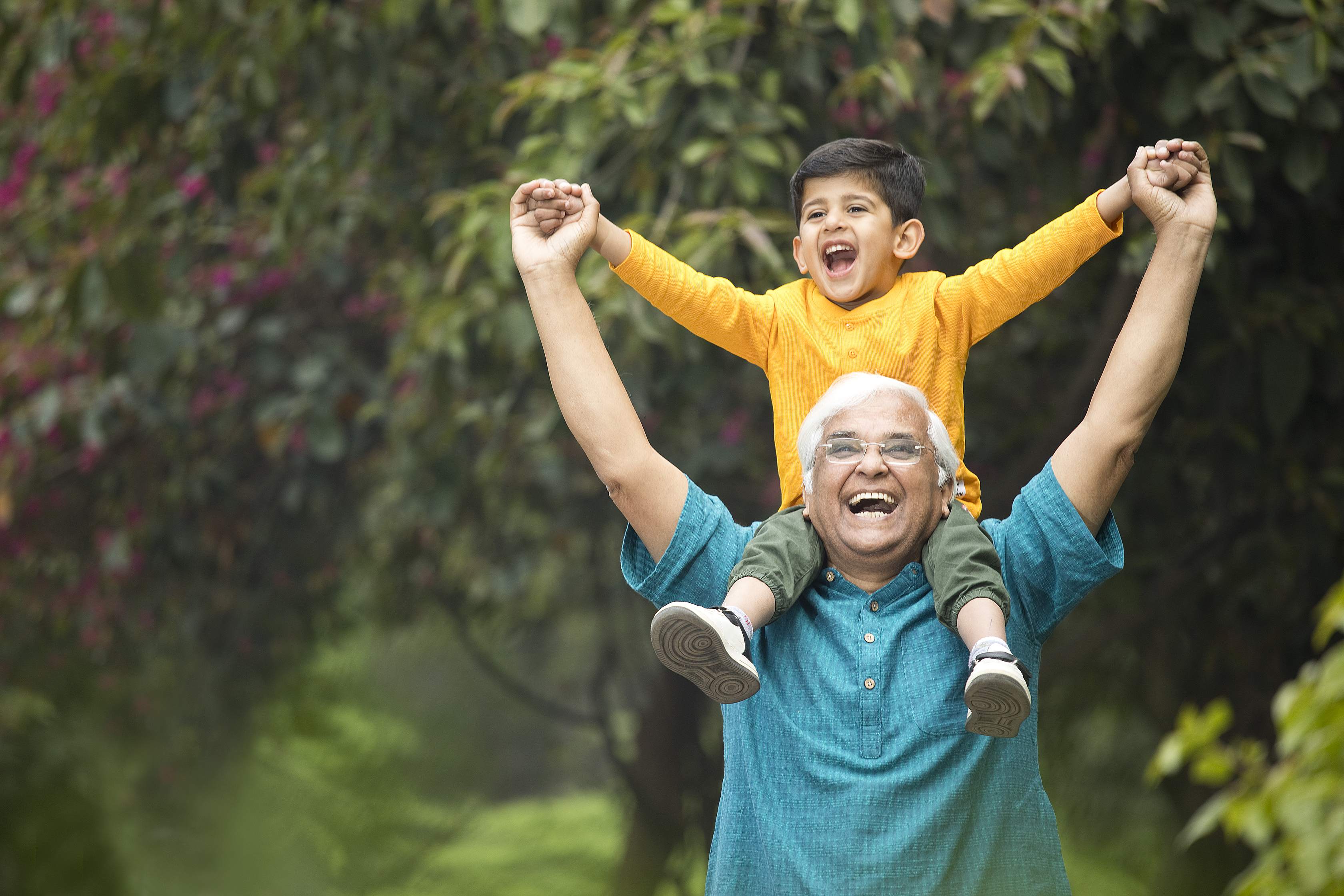 Happy grandfather carrying grandson on shoulders outdoors celebrating together