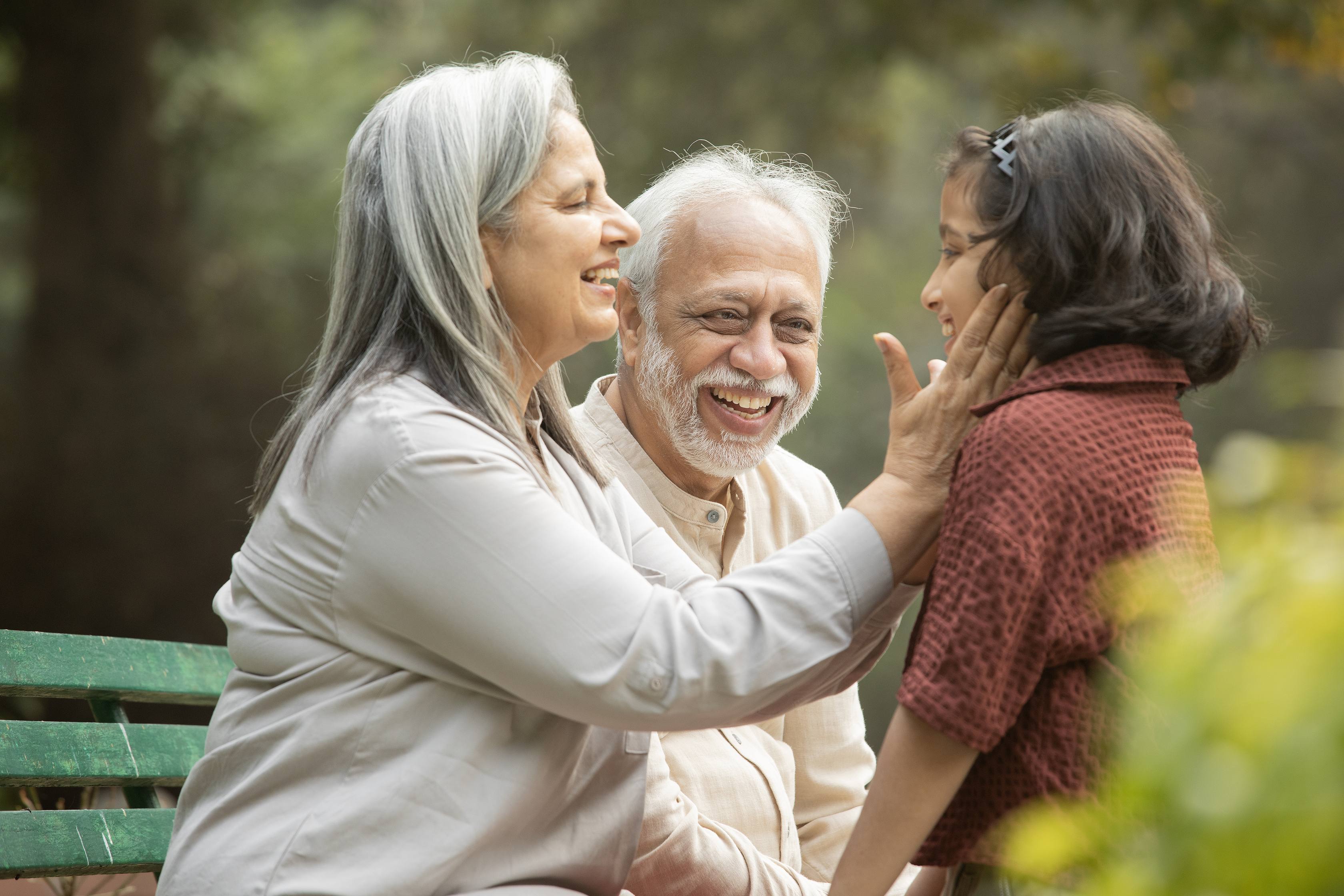 Happy grandparents playing with granddaughter in park on sunny day