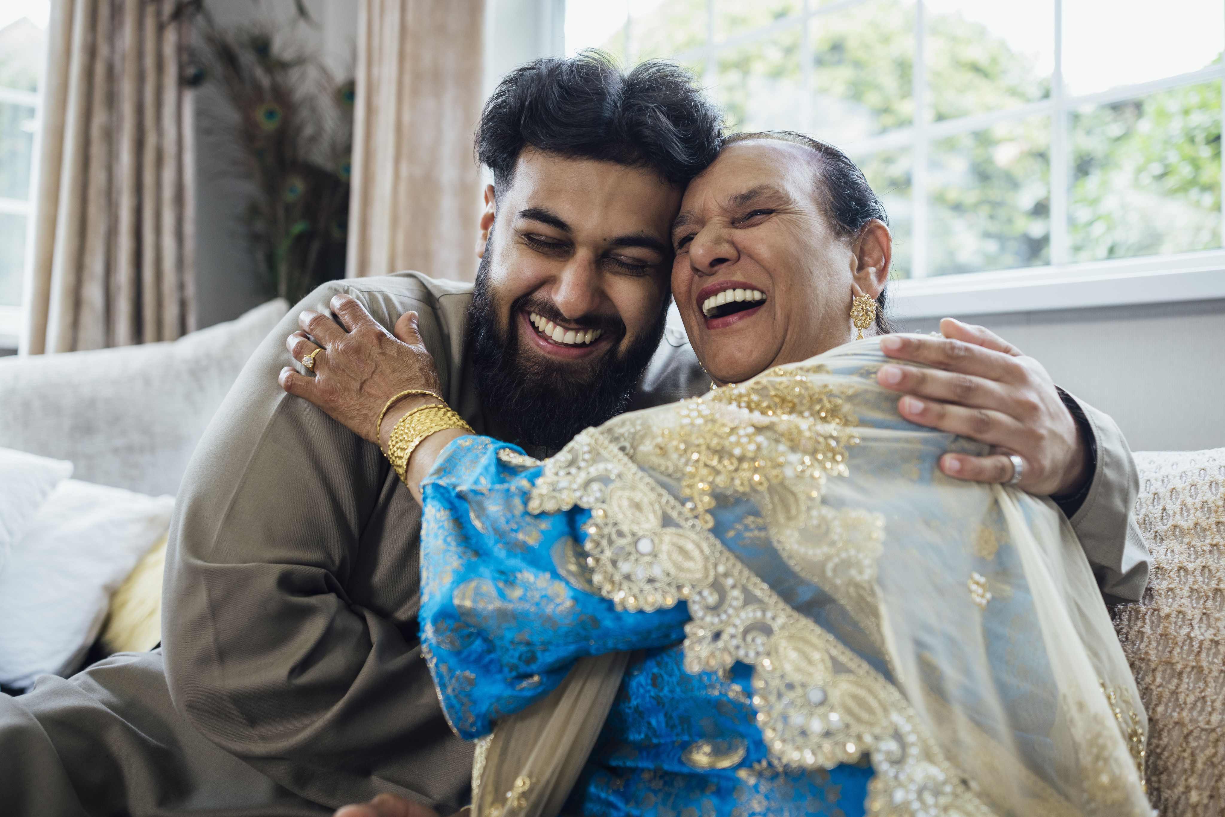 Happy young man and elderly woman embracing warmly in traditional attire