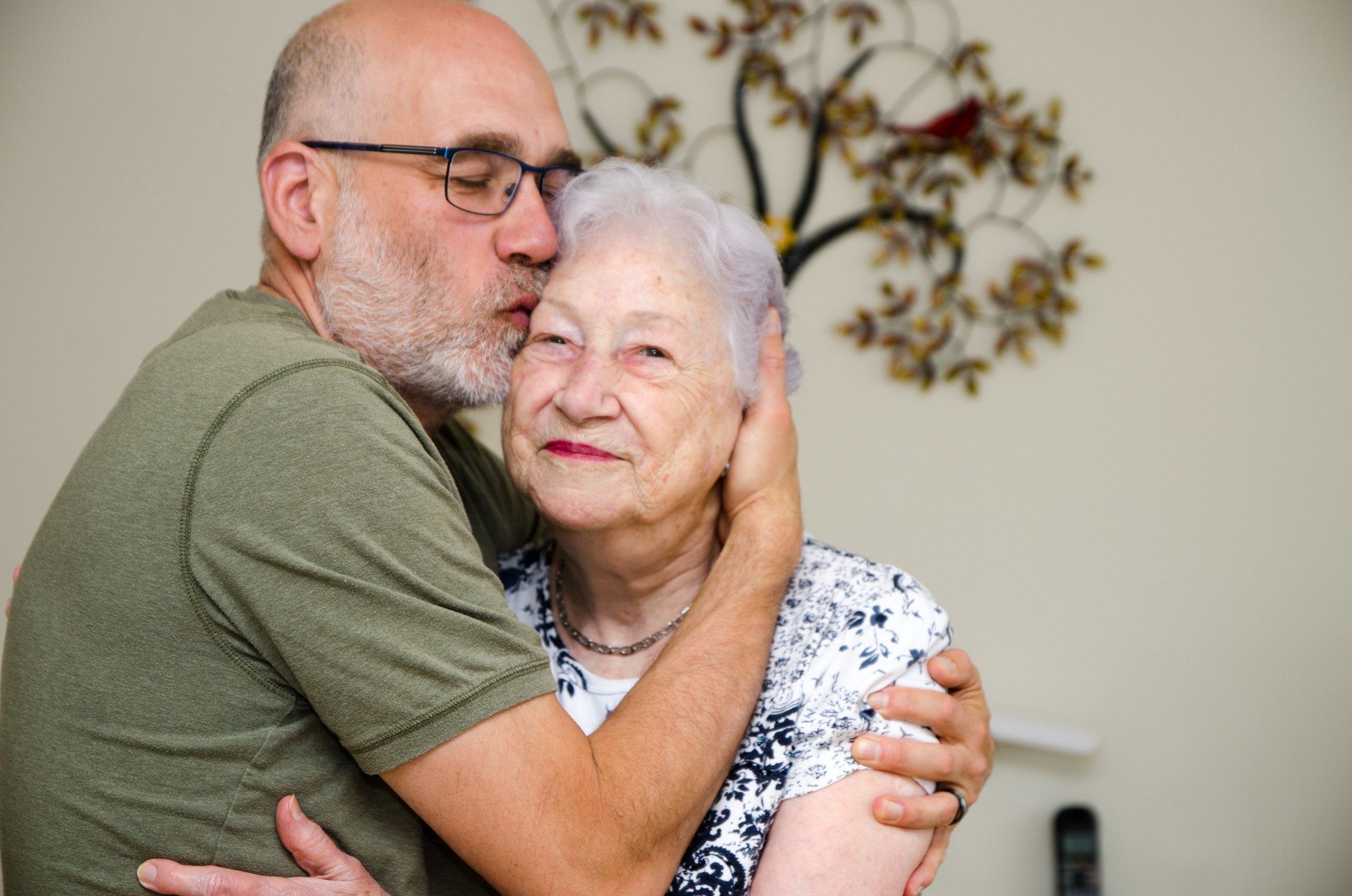 Middle-aged man kissing elderly woman's forehead in loving embrace