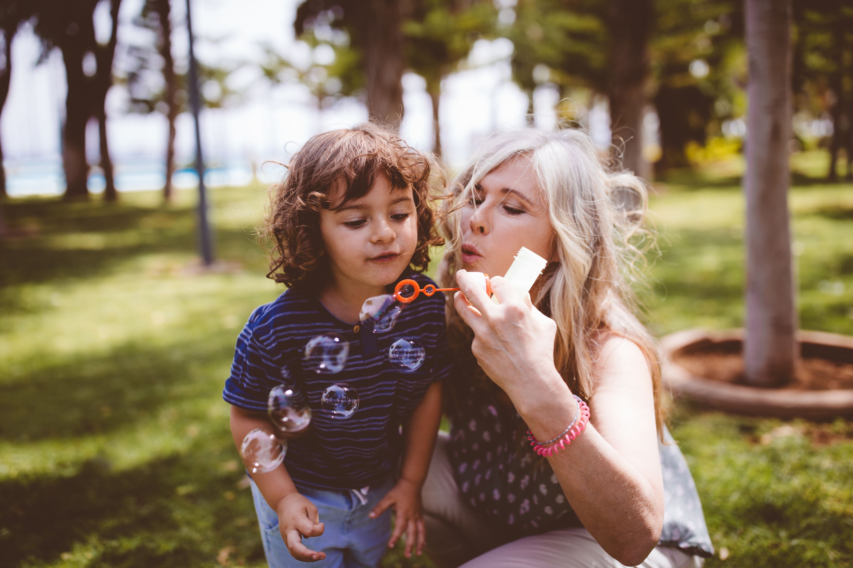 Mother and child blowing bubbles together in sunny park