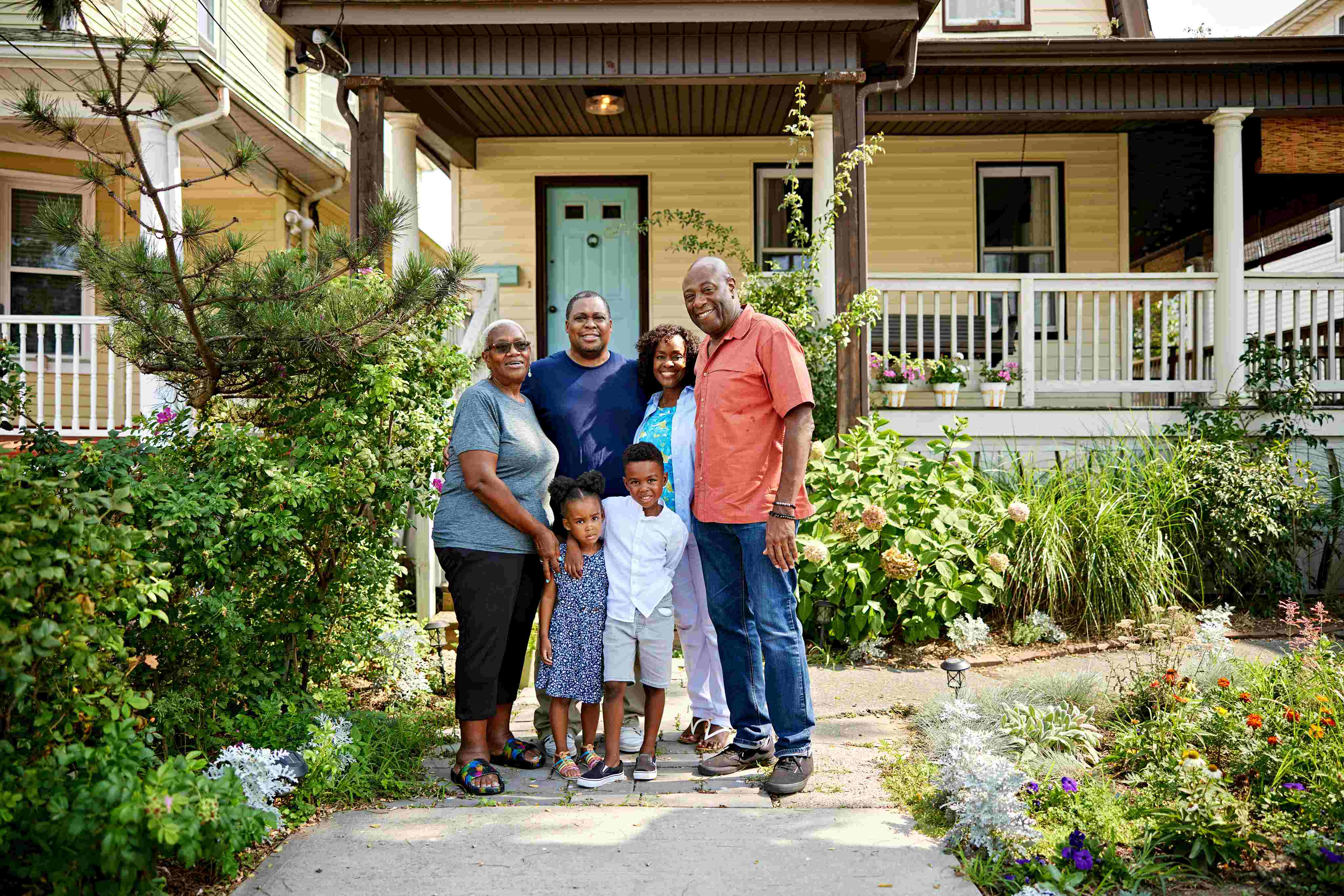 Multi-generational African American family posing in front of yellow house with garden