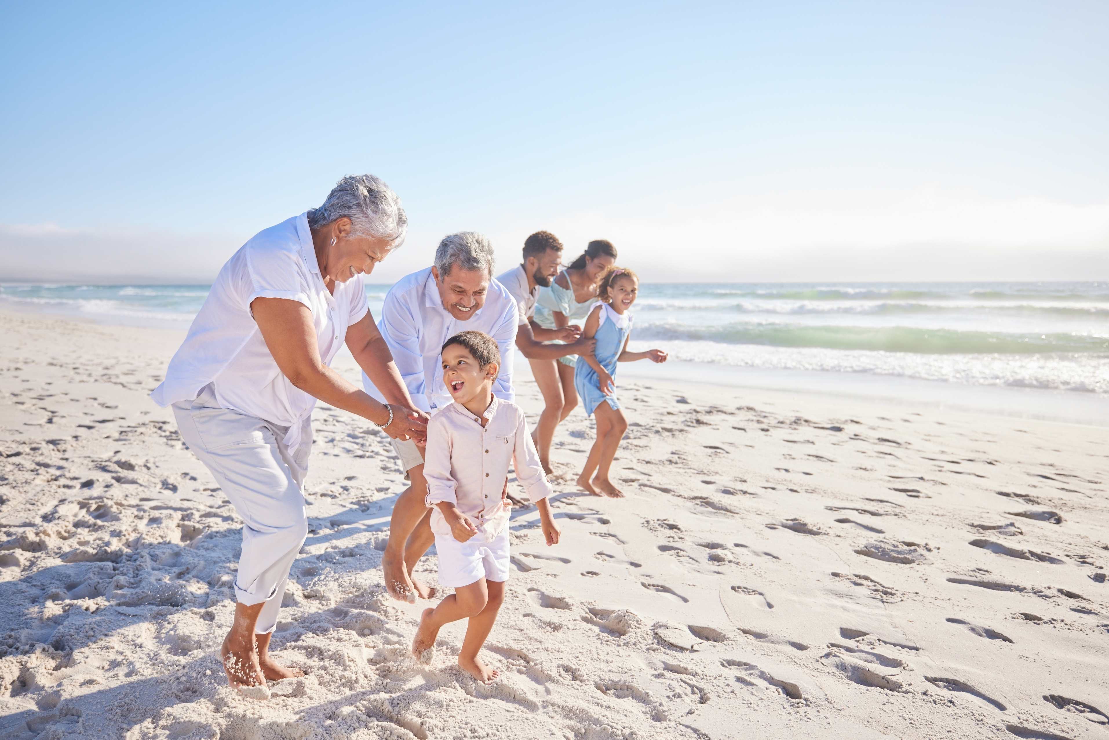 Multi-generational family playing and running together on sunny beach