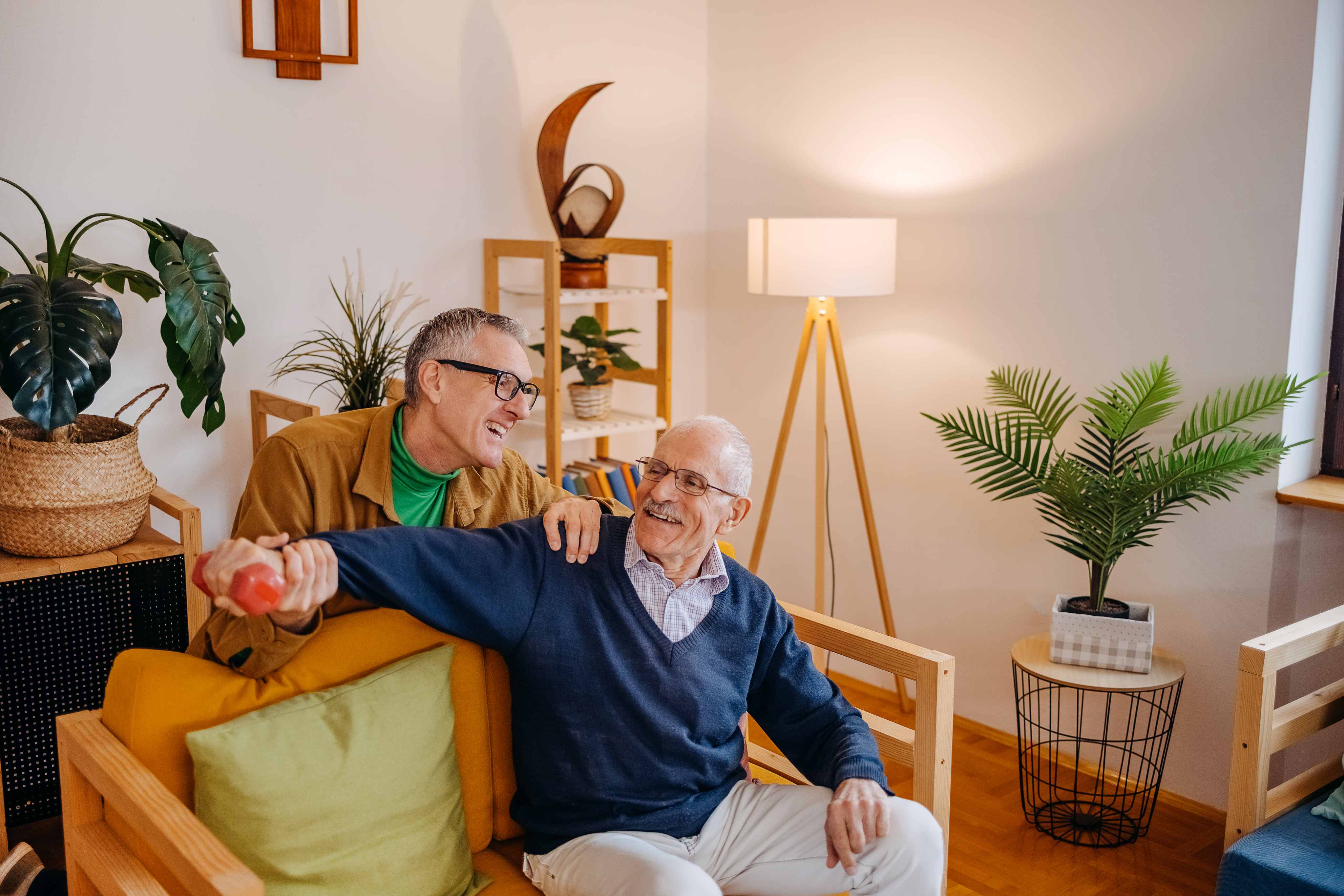 Senior man exercising with dumbbell while caregiver assists in living room
