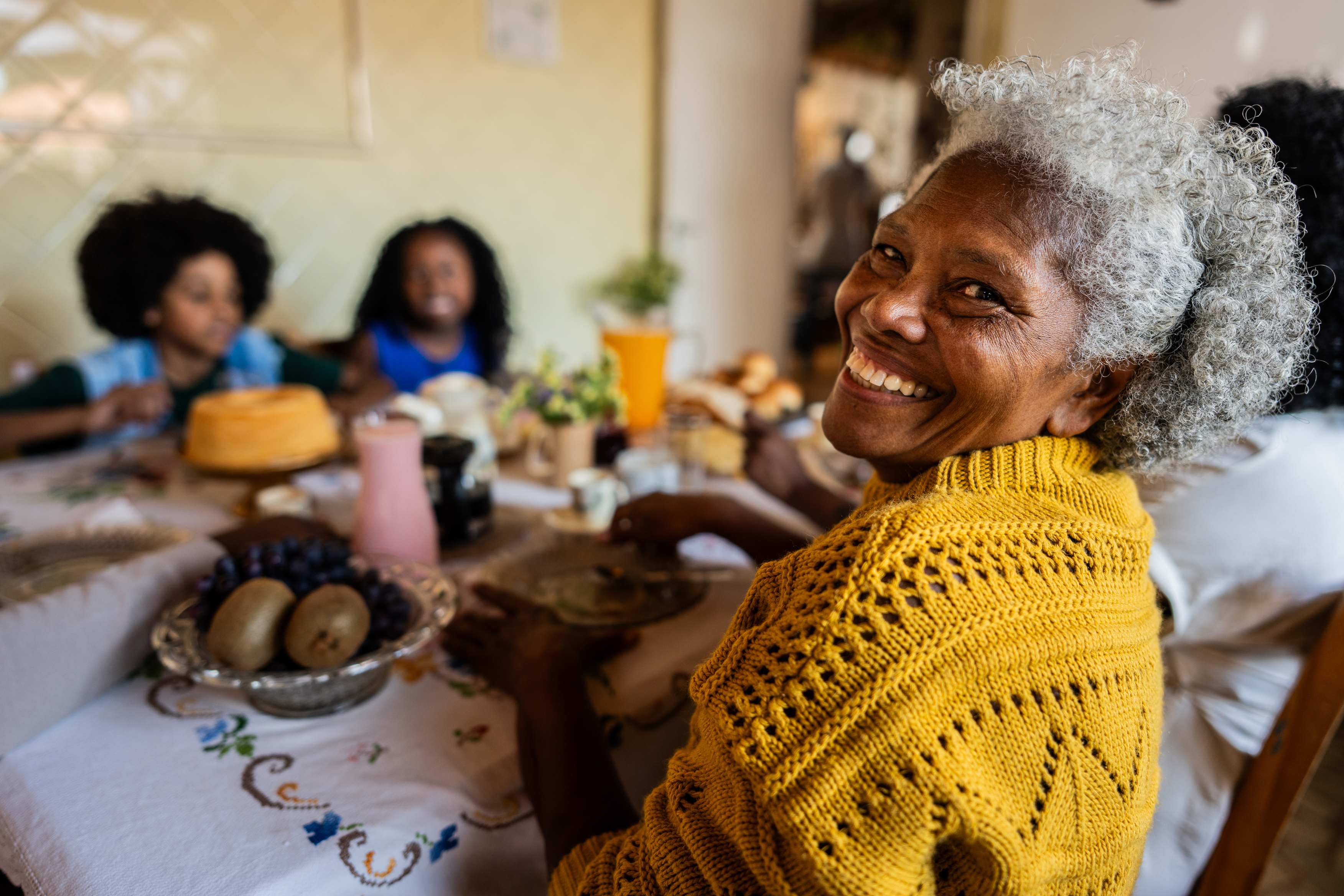Smiling elderly woman in yellow sweater at family dinner table