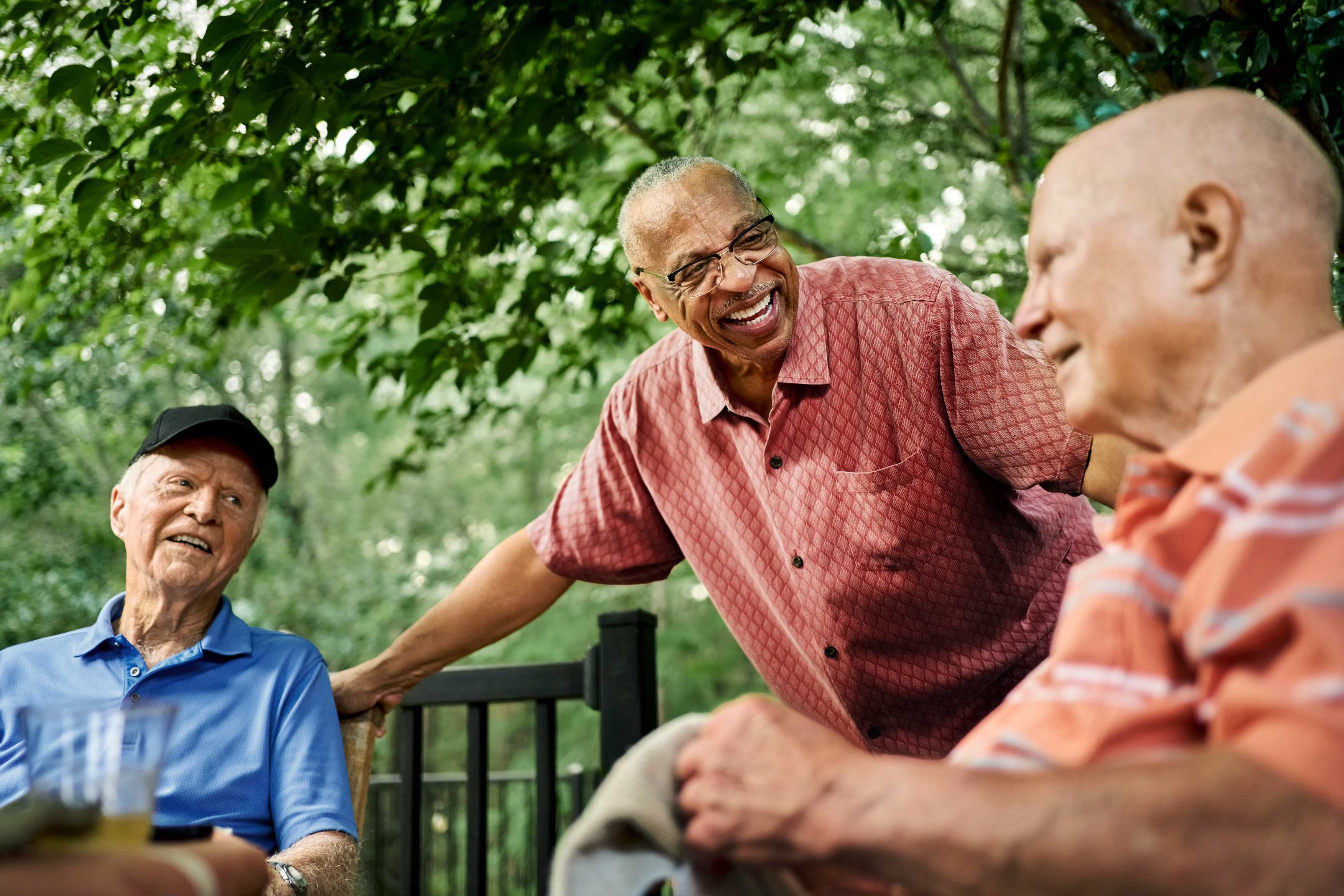 Three elderly men enjoying conversation outdoors under green trees