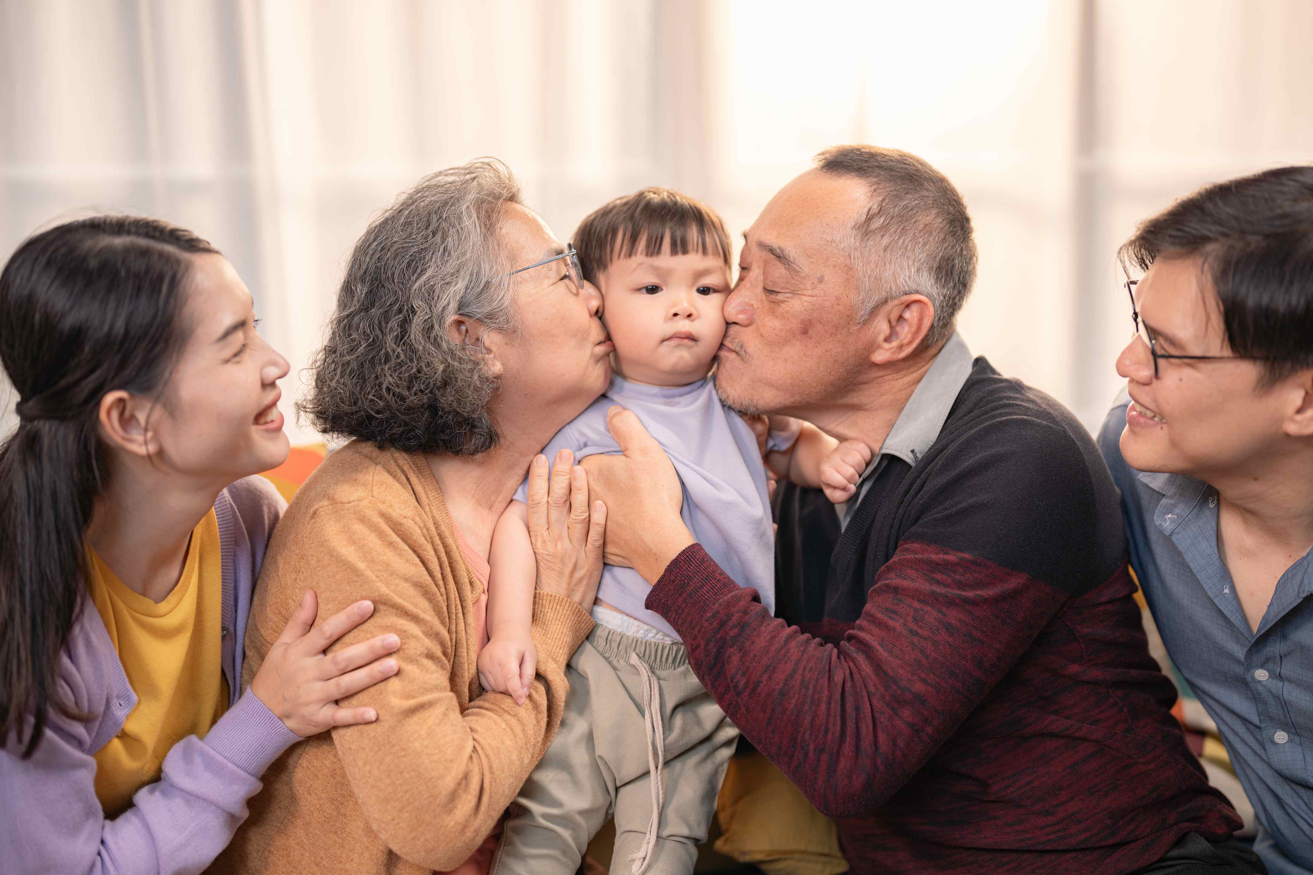 Three generation Asian family kissing toddler in warm indoor setting