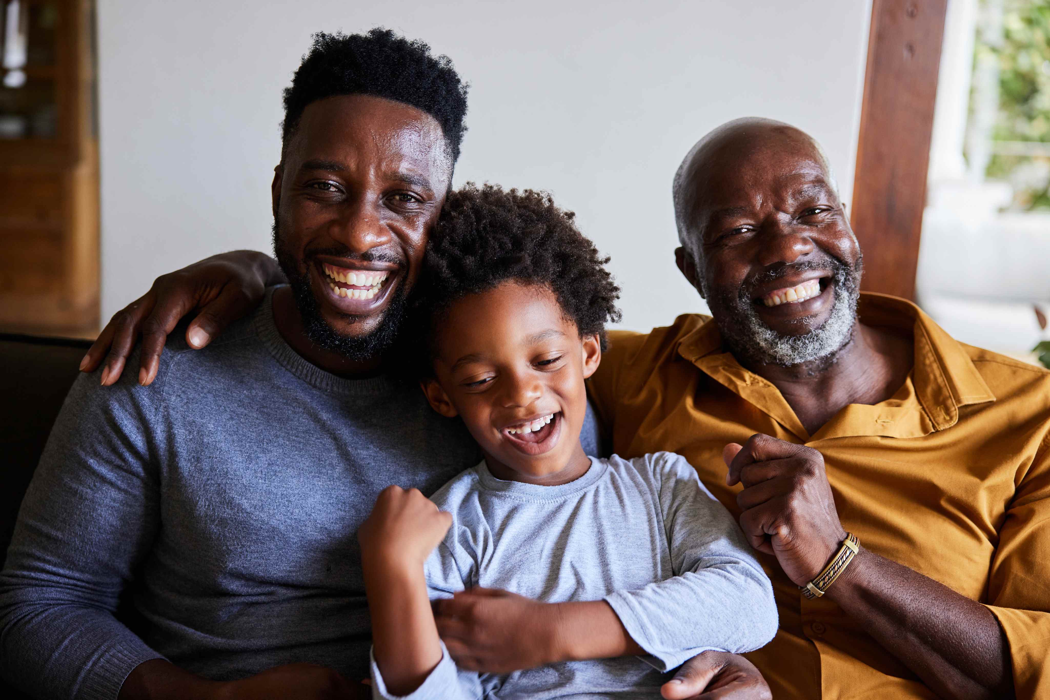 Three generations of Black men smiling together on a couch