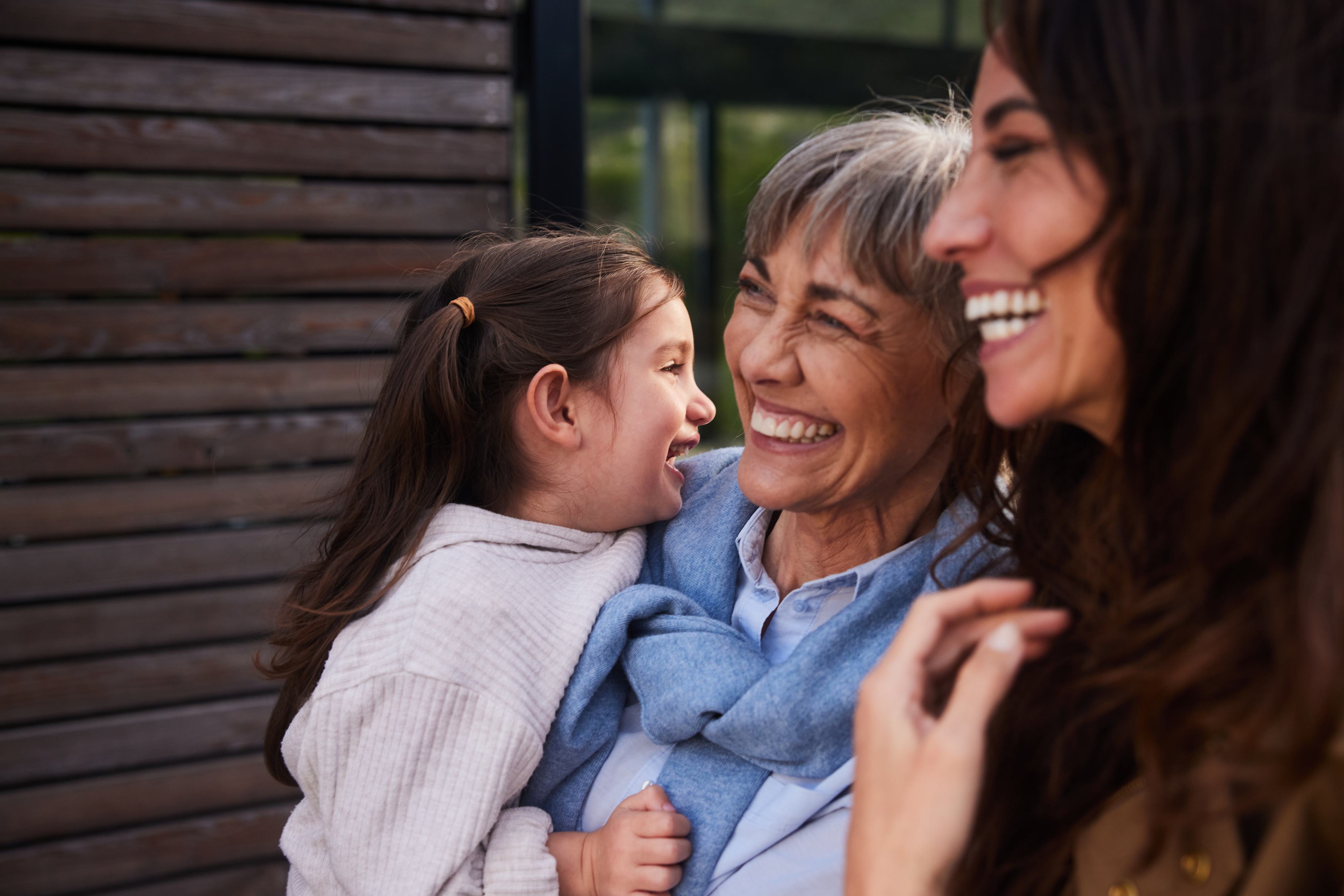 Three generations of women laughing and embracing outdoors
