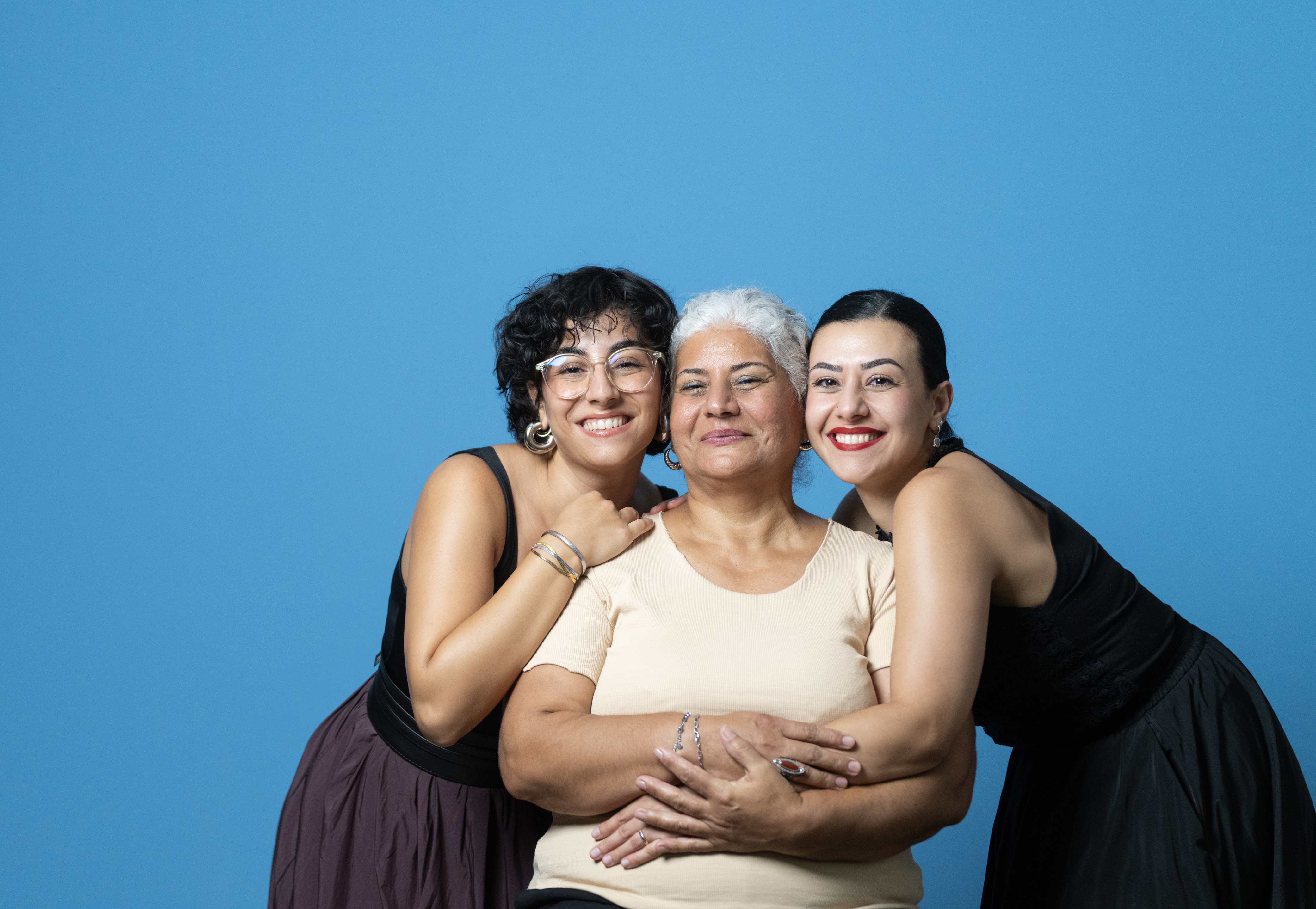 Three generations of women smiling together against blue background