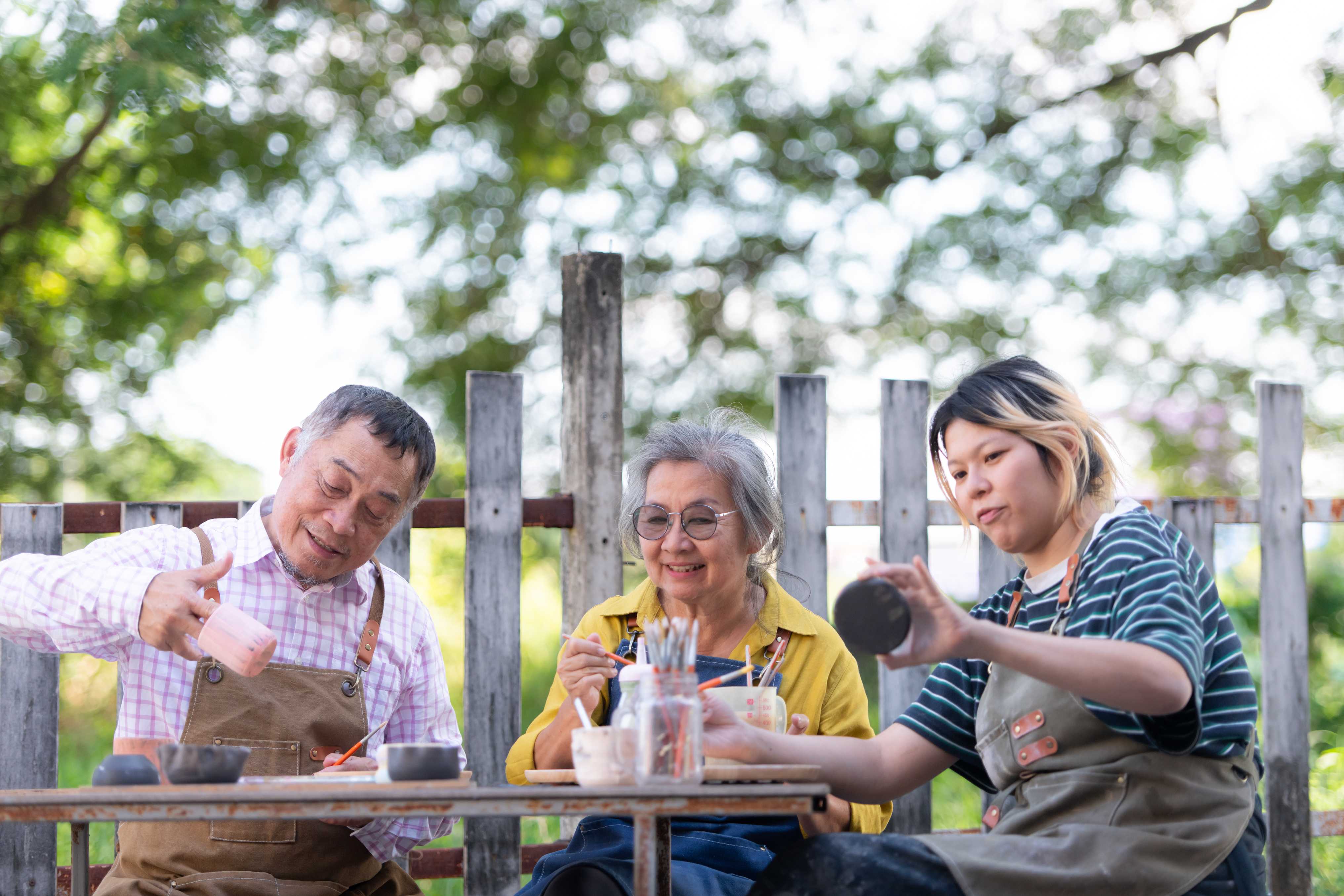 Three people in aprons enjoying beverages at outdoor wooden table