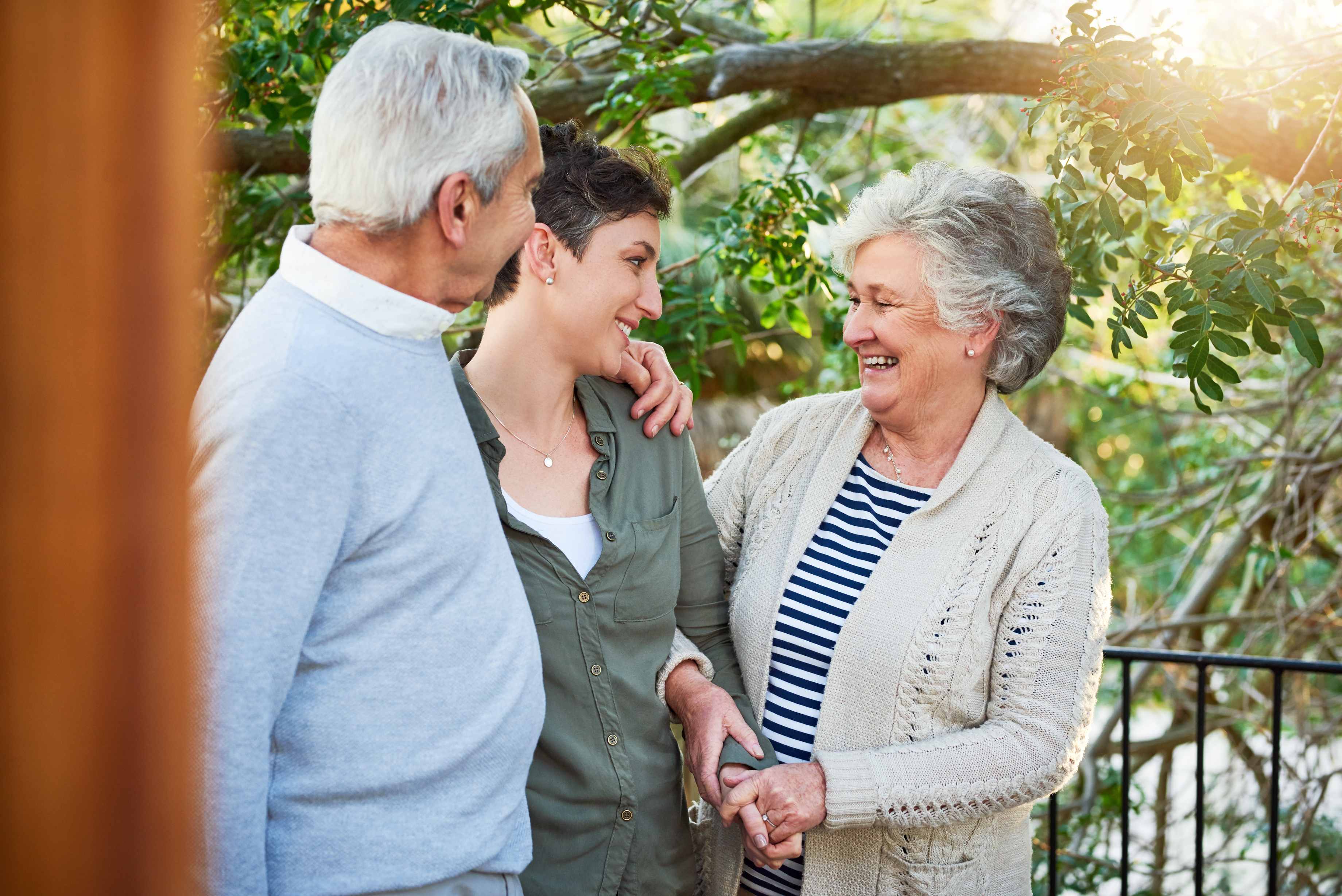 Three people smiling together outdoors in garden setting with sunlight