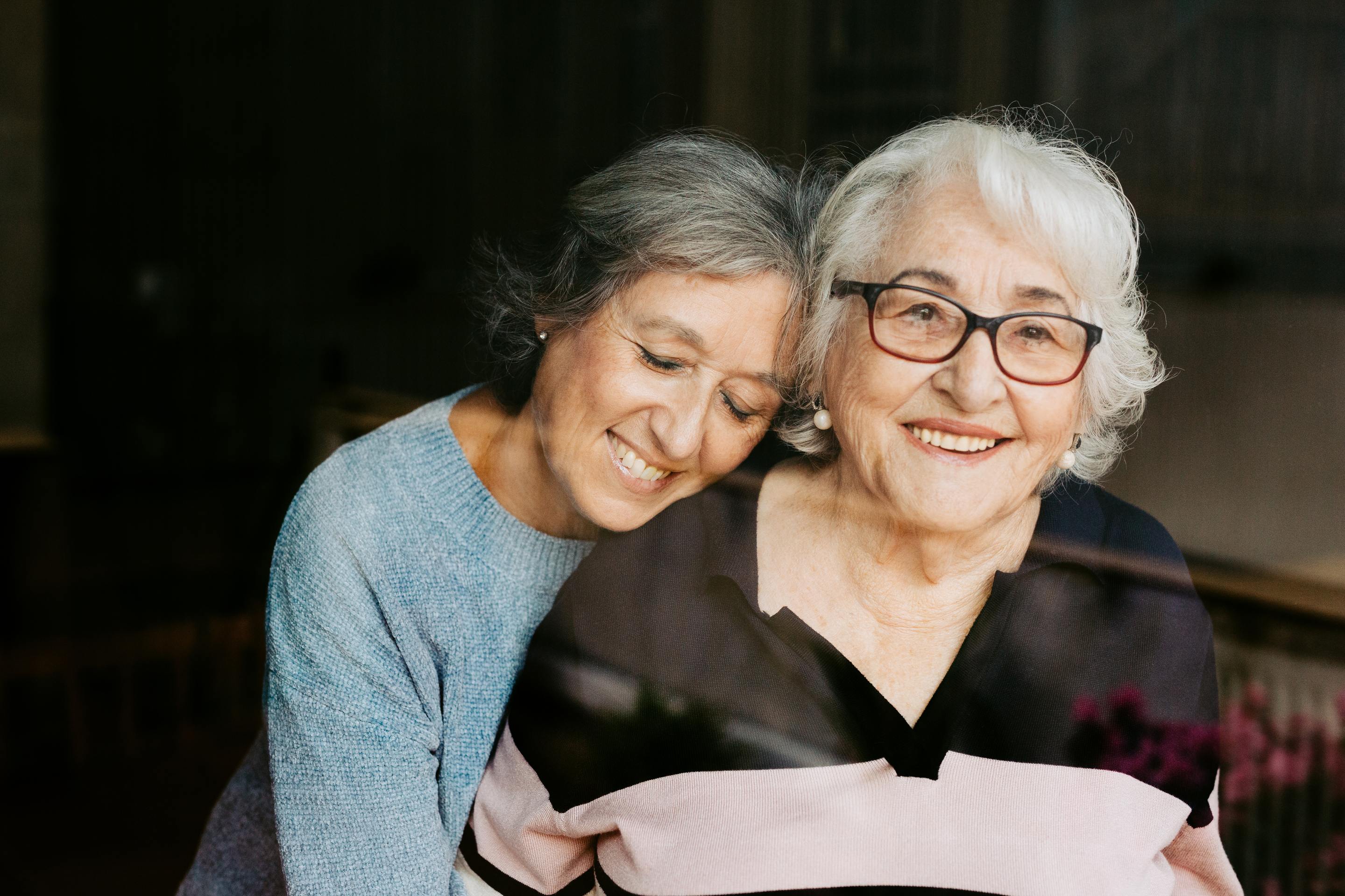 Two elderly women embracing and smiling warmly together