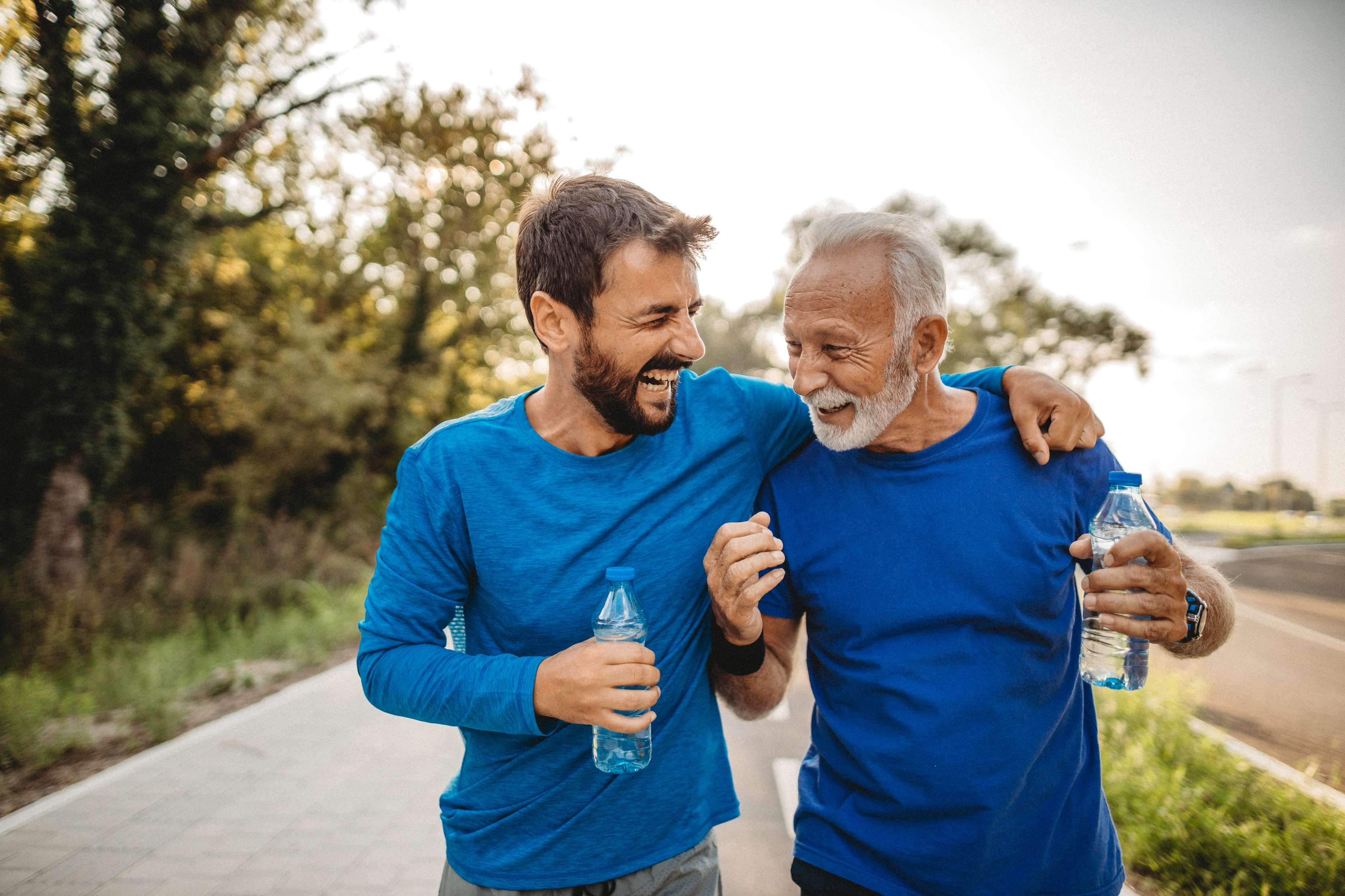 Two men in blue shirts exercising together outdoors with water bottles