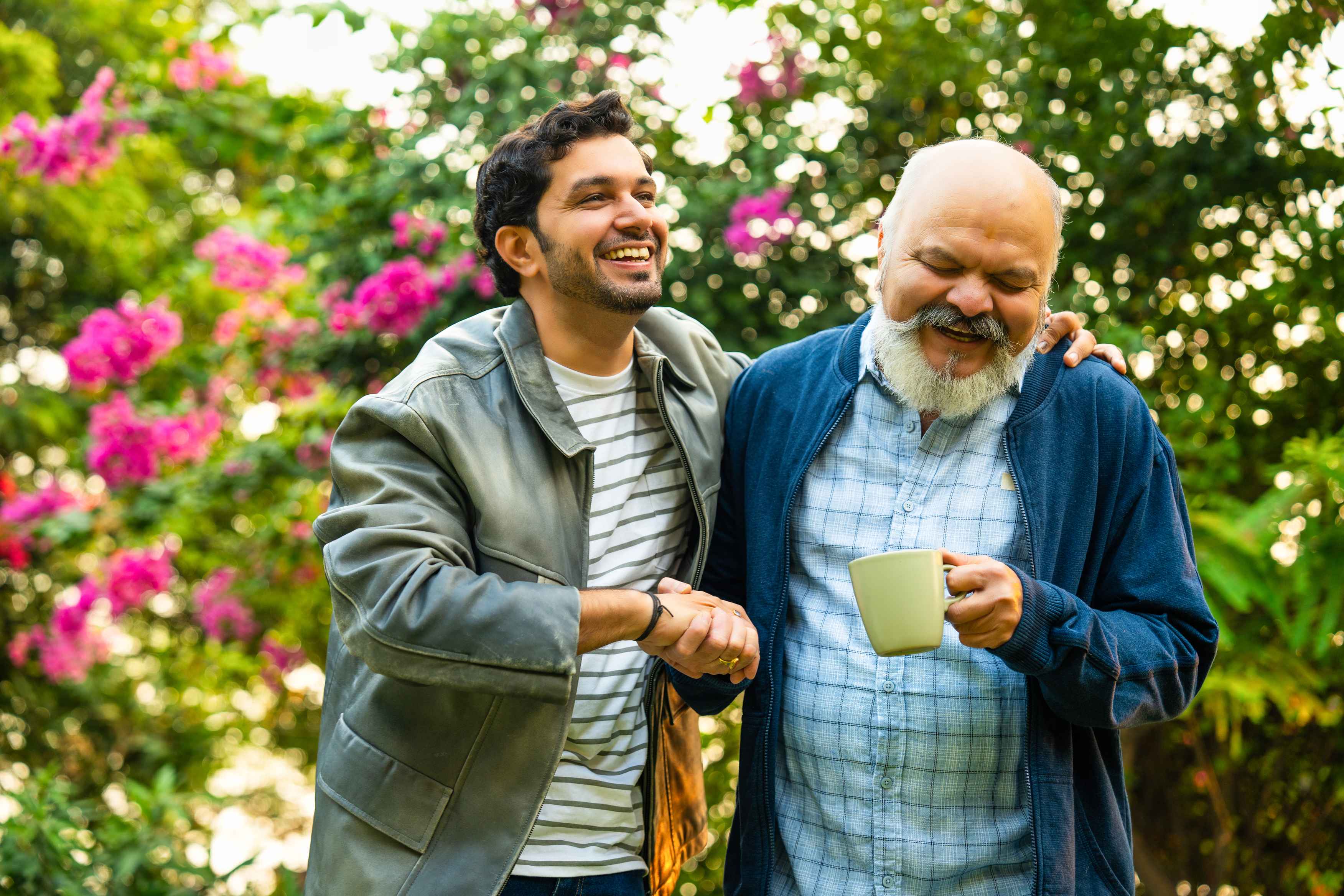 Two men laughing together in garden with pink flowers