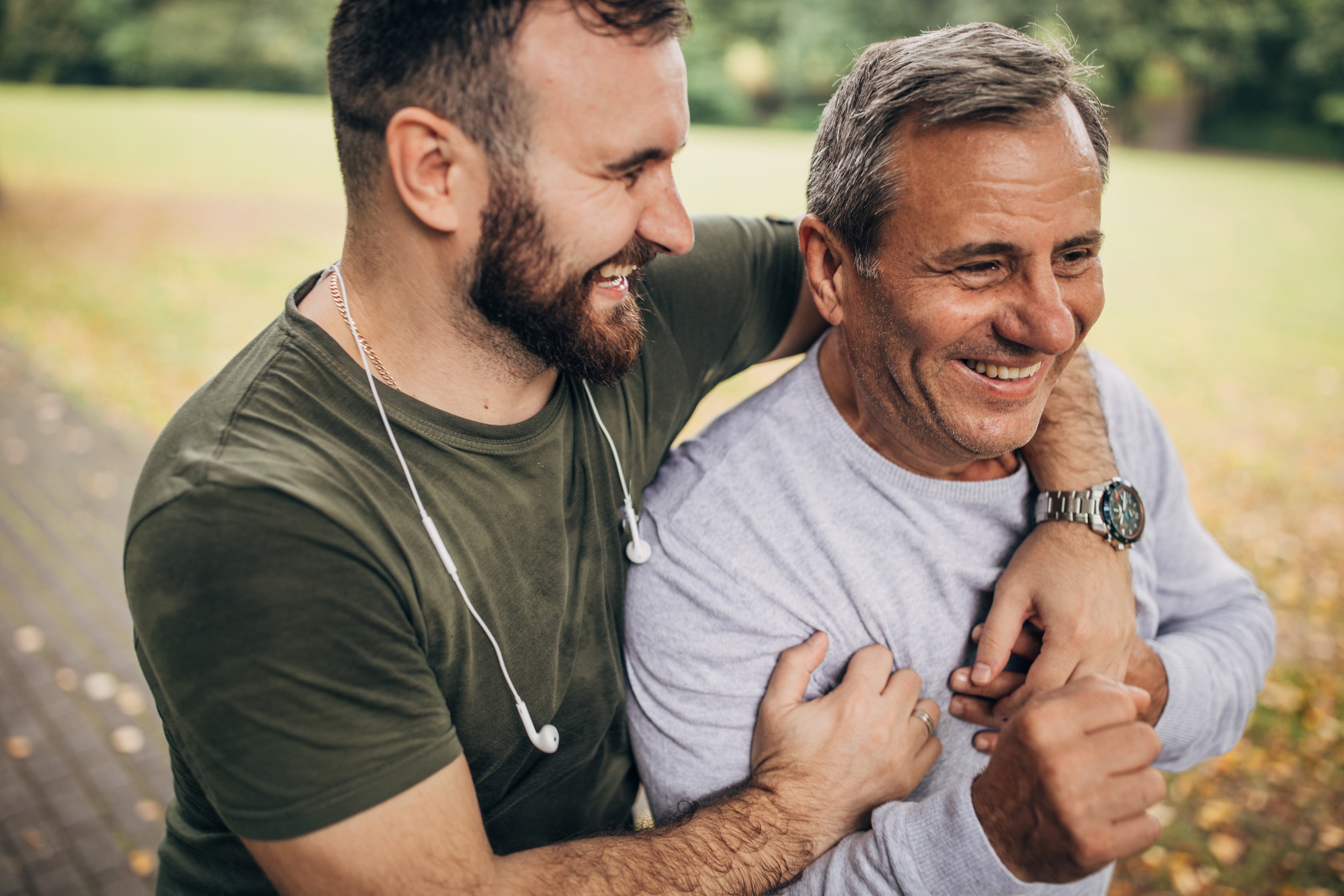 Two men smiling and embracing outdoors in natural setting