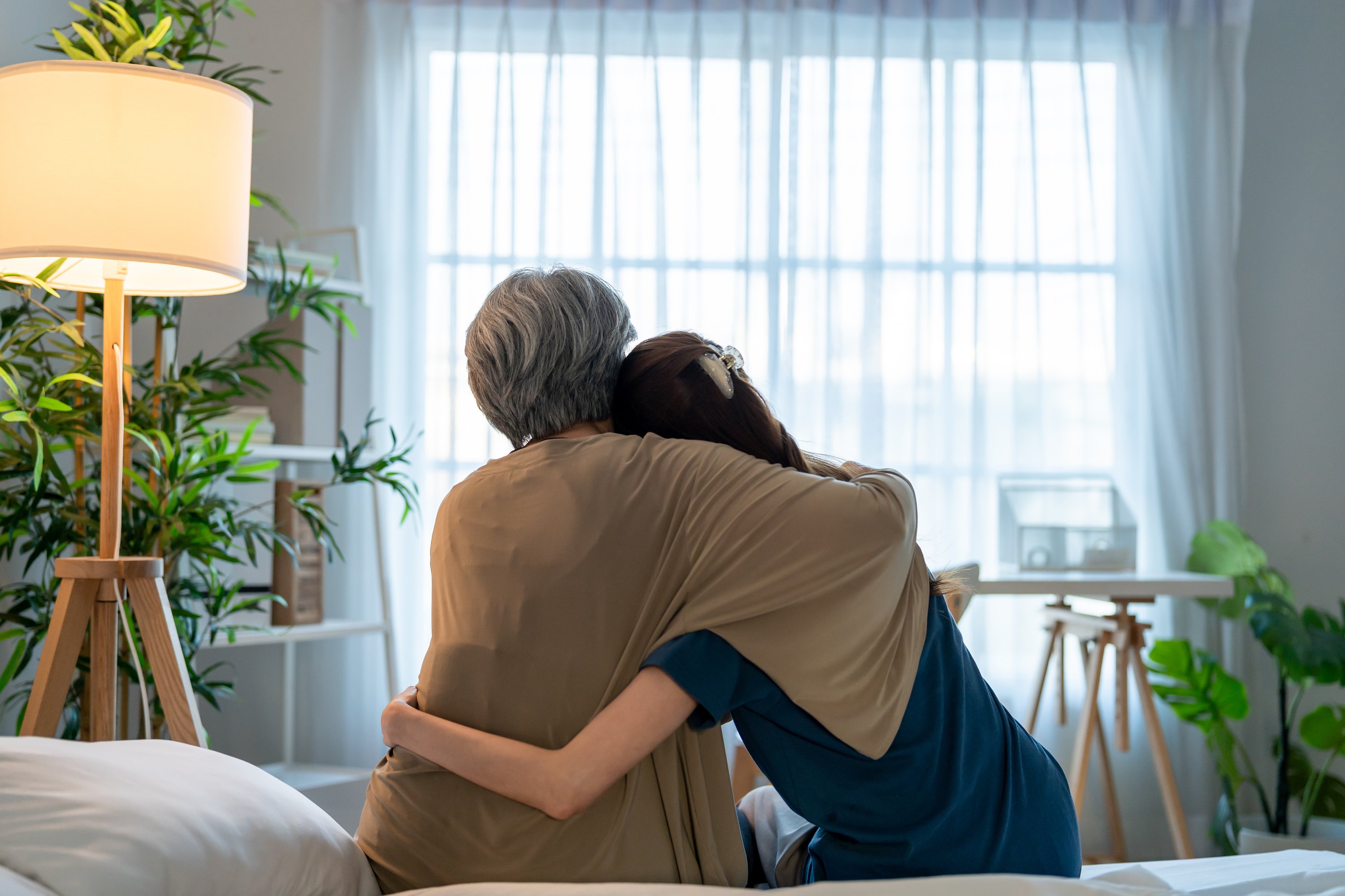 Two people embracing in a bright room with plants