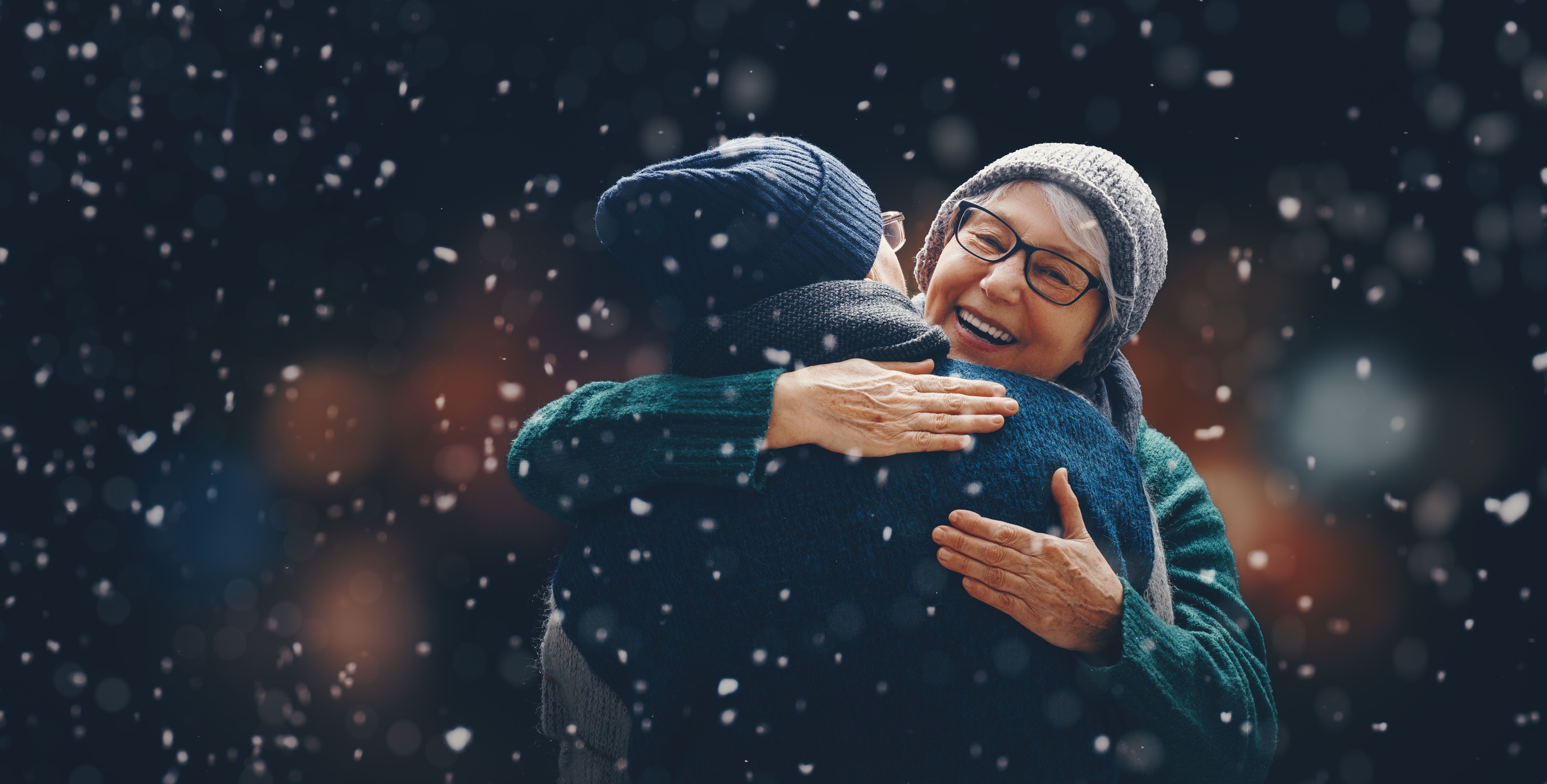 Two people embracing warmly in falling snow wearing winter clothing