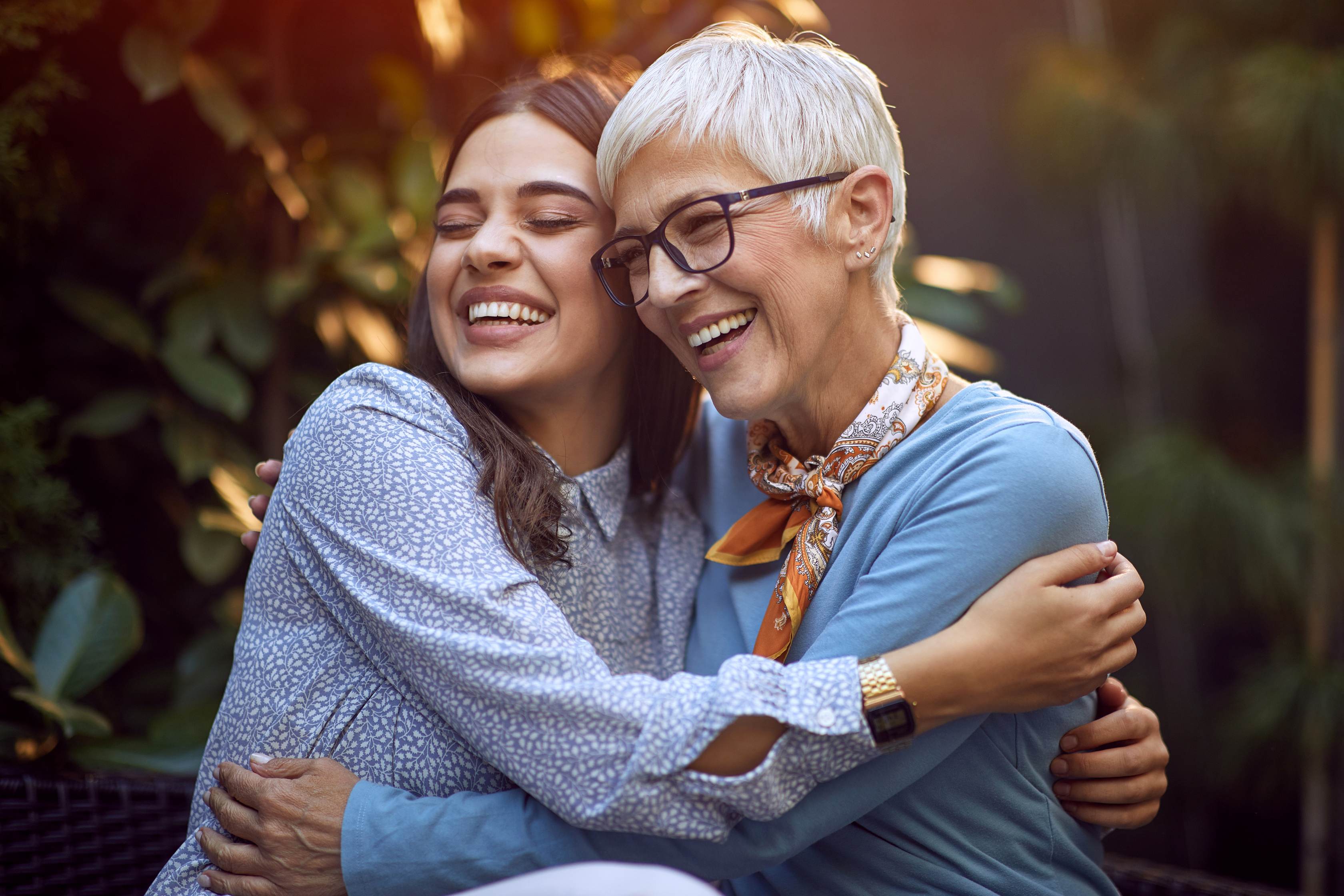 Two women embracing and smiling outdoors in warm autumn light