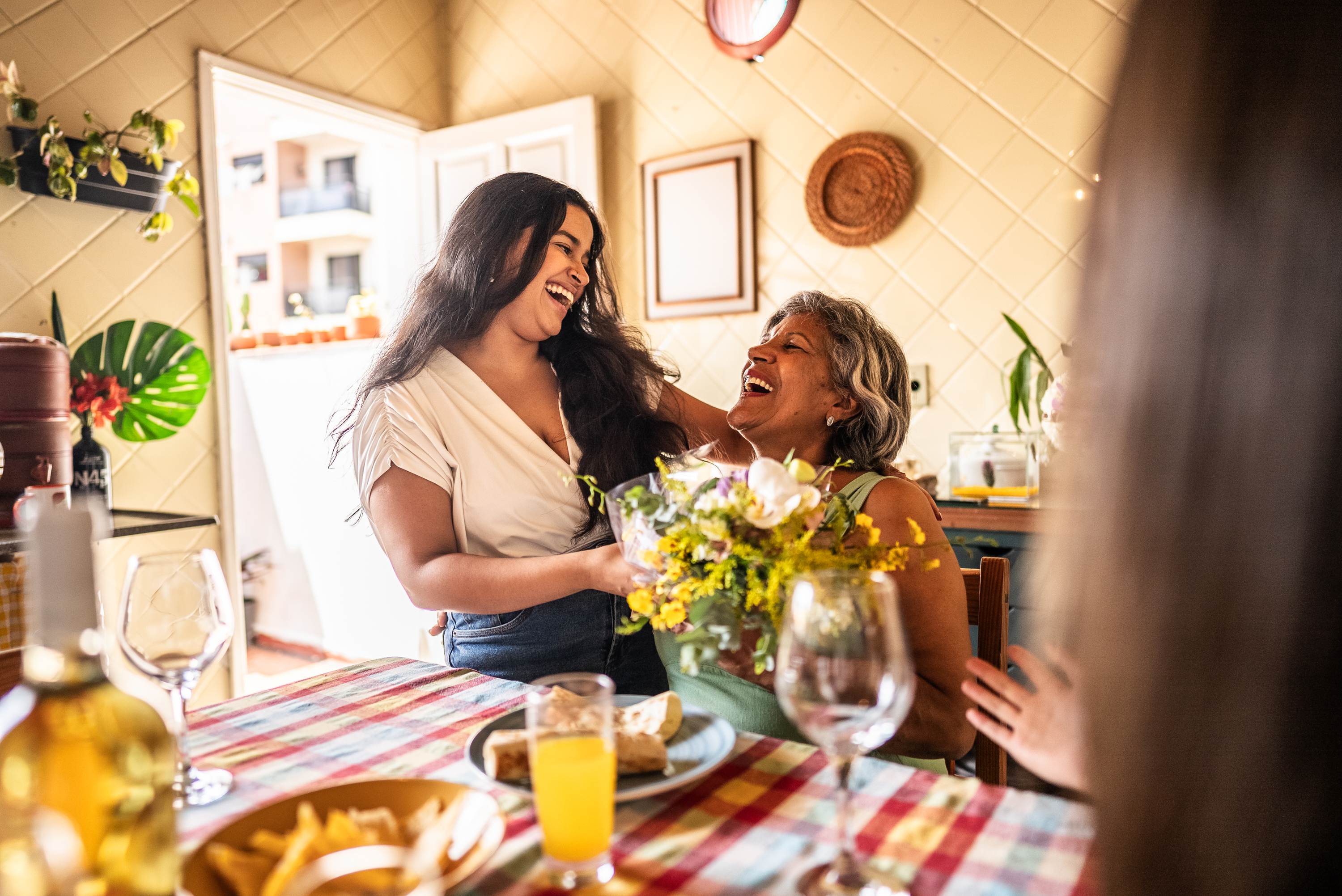 Two women laughing together at dining table with flowers and wine