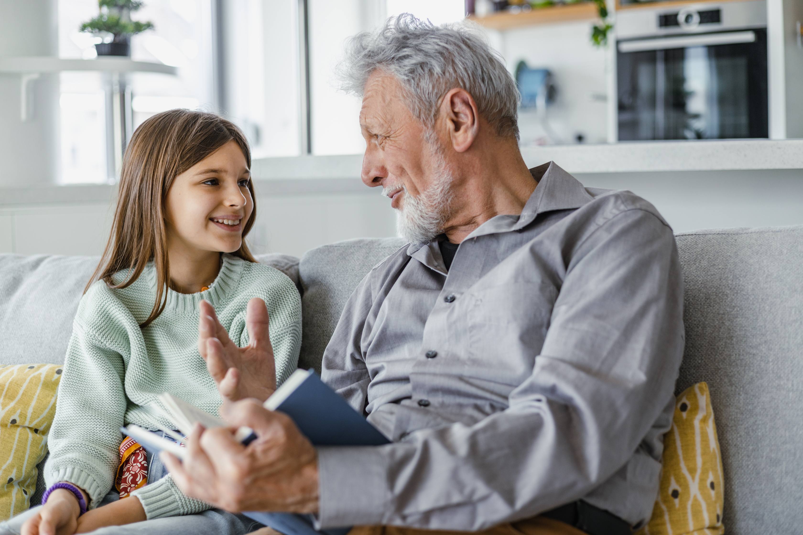 Young girl and grandfather talking on couch in modern kitchen