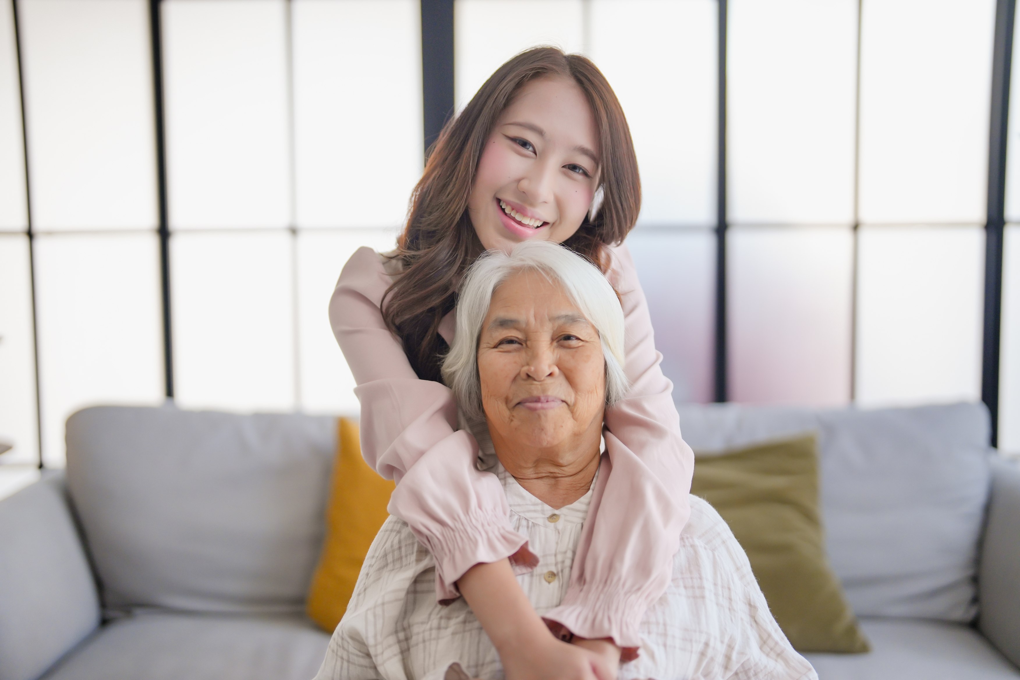 Young woman embracing elderly grandmother on couch in bright living room