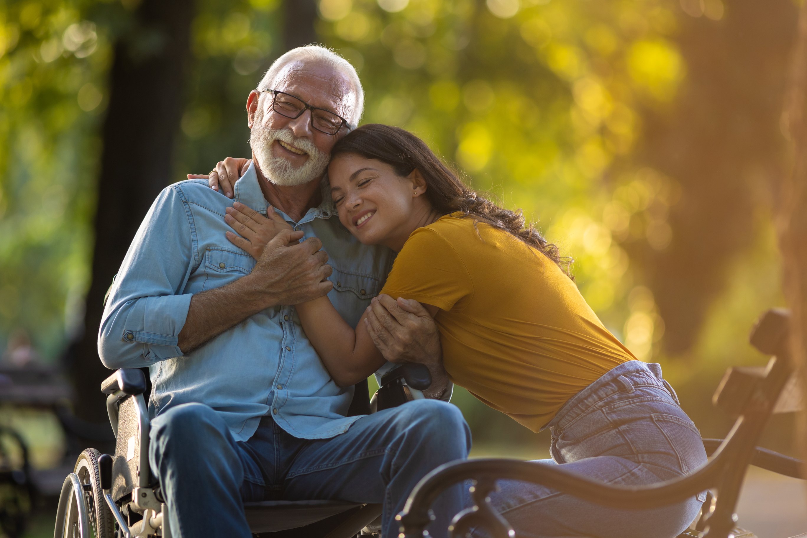 Young woman embracing elderly man in wheelchair outdoors during golden hour